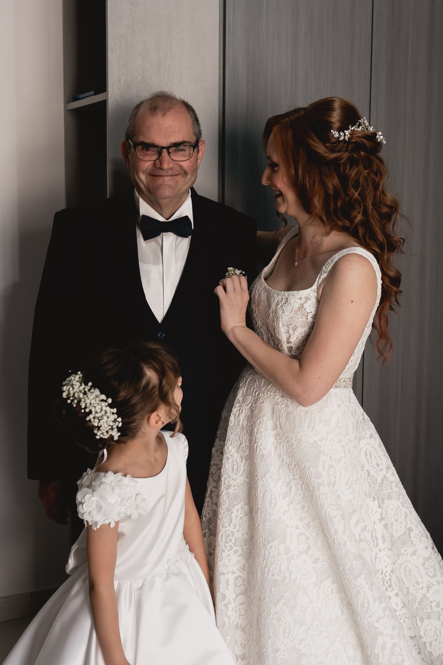 Three people share a joyful moment in formal attire at a wedding celebration.