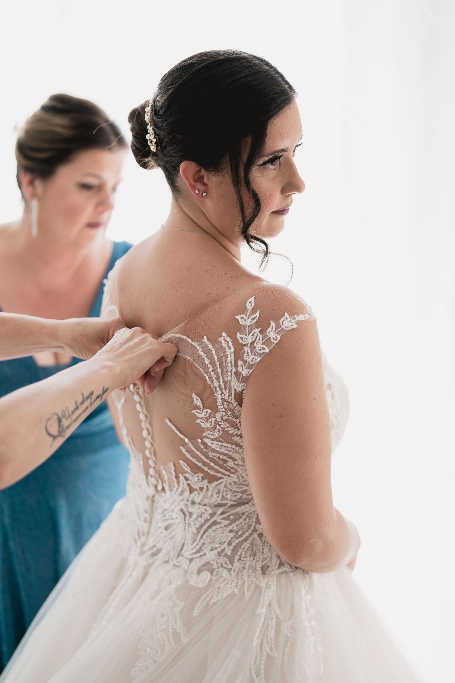 An elegant lace wedding dress with intricate floral details being buttoned up on a bride.