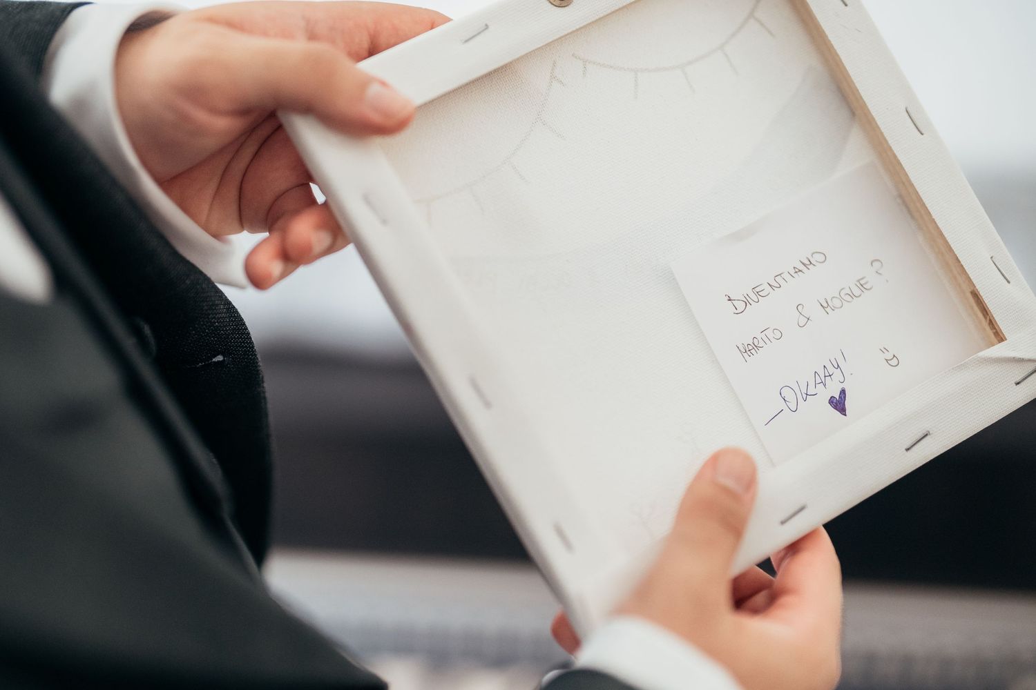 Hands holding a small framed item with handwritten text visible.