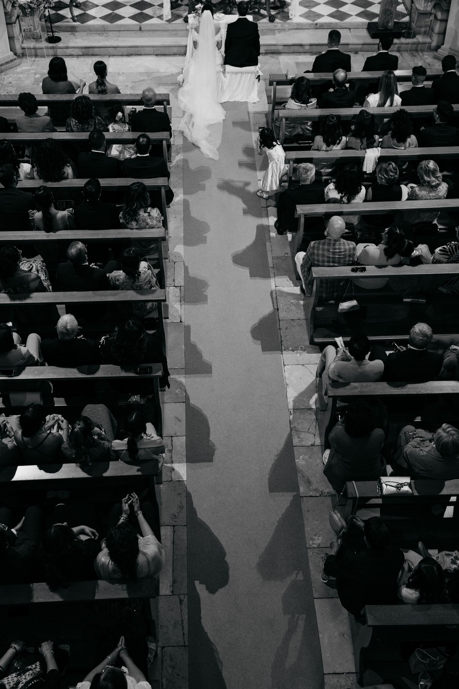 Overhead black and white view of a church wedding ceremony showing guests seated in wooden pews.