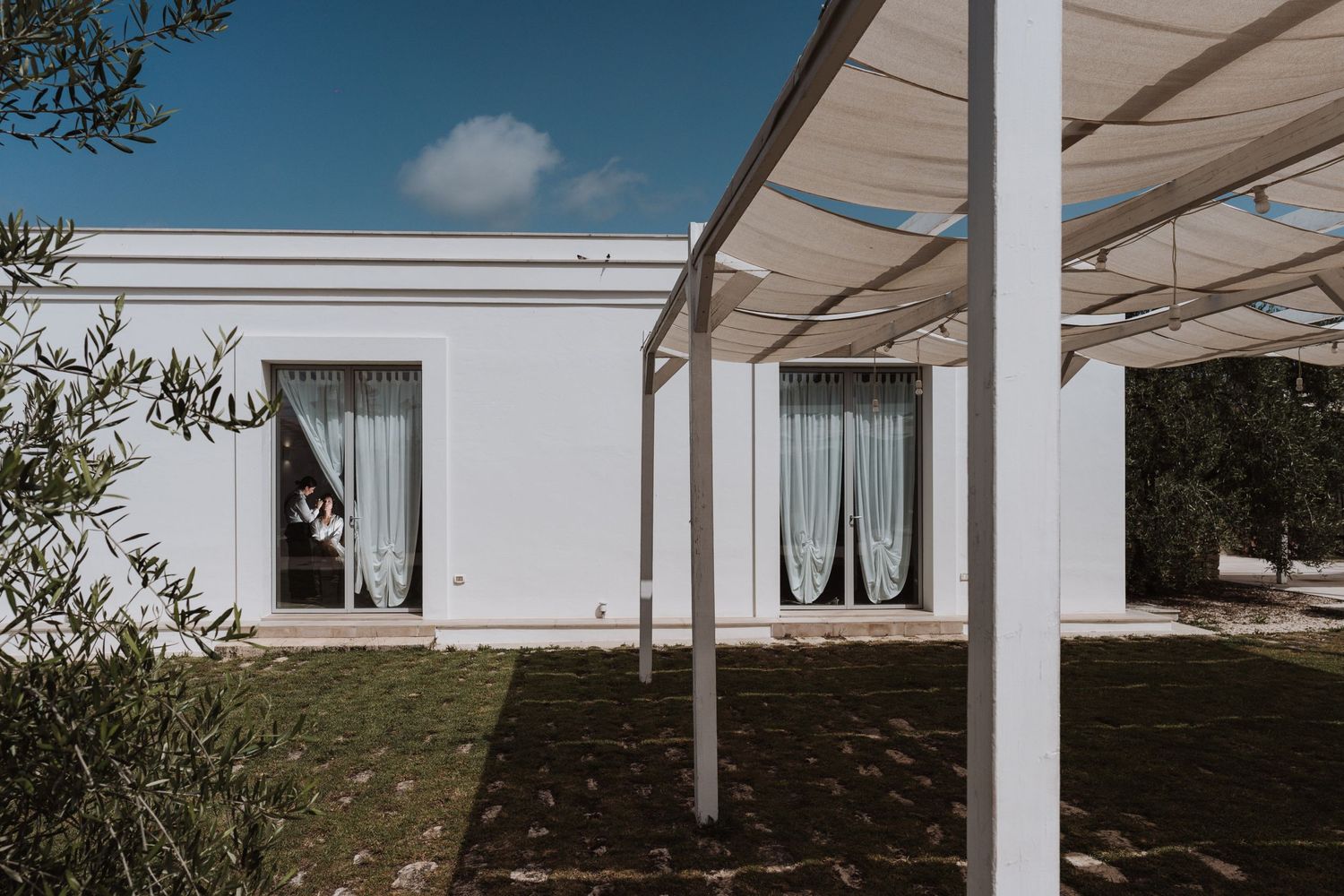 Modern white building exterior with covered patio and sheer curtained windows.