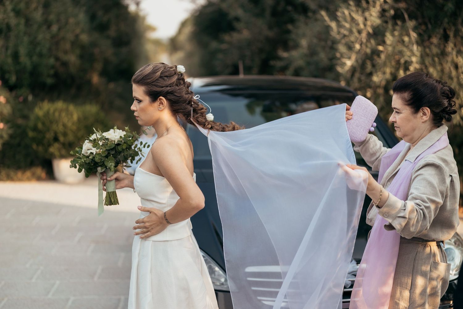 Wedding preparation moment with flowing veil adjustment on a country road.
