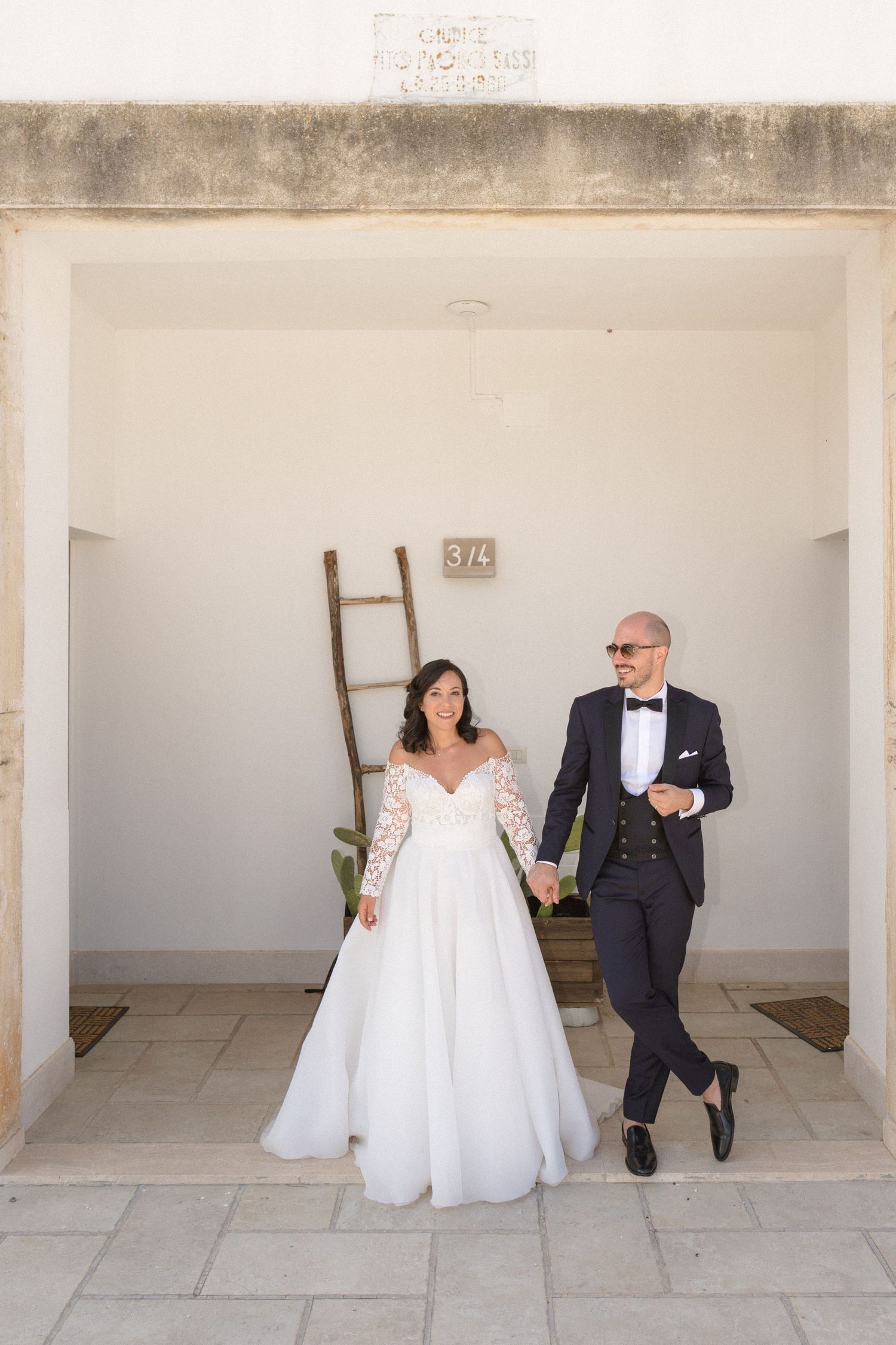 Creative wedding portrait series showing couple sitting against minimalist white wall backdrop.