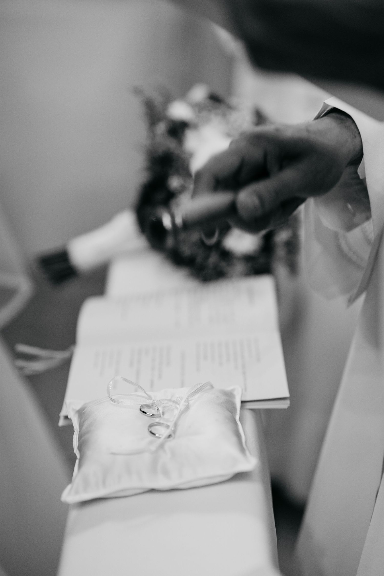 Close-up view of hands signing wedding documents in black and white.
