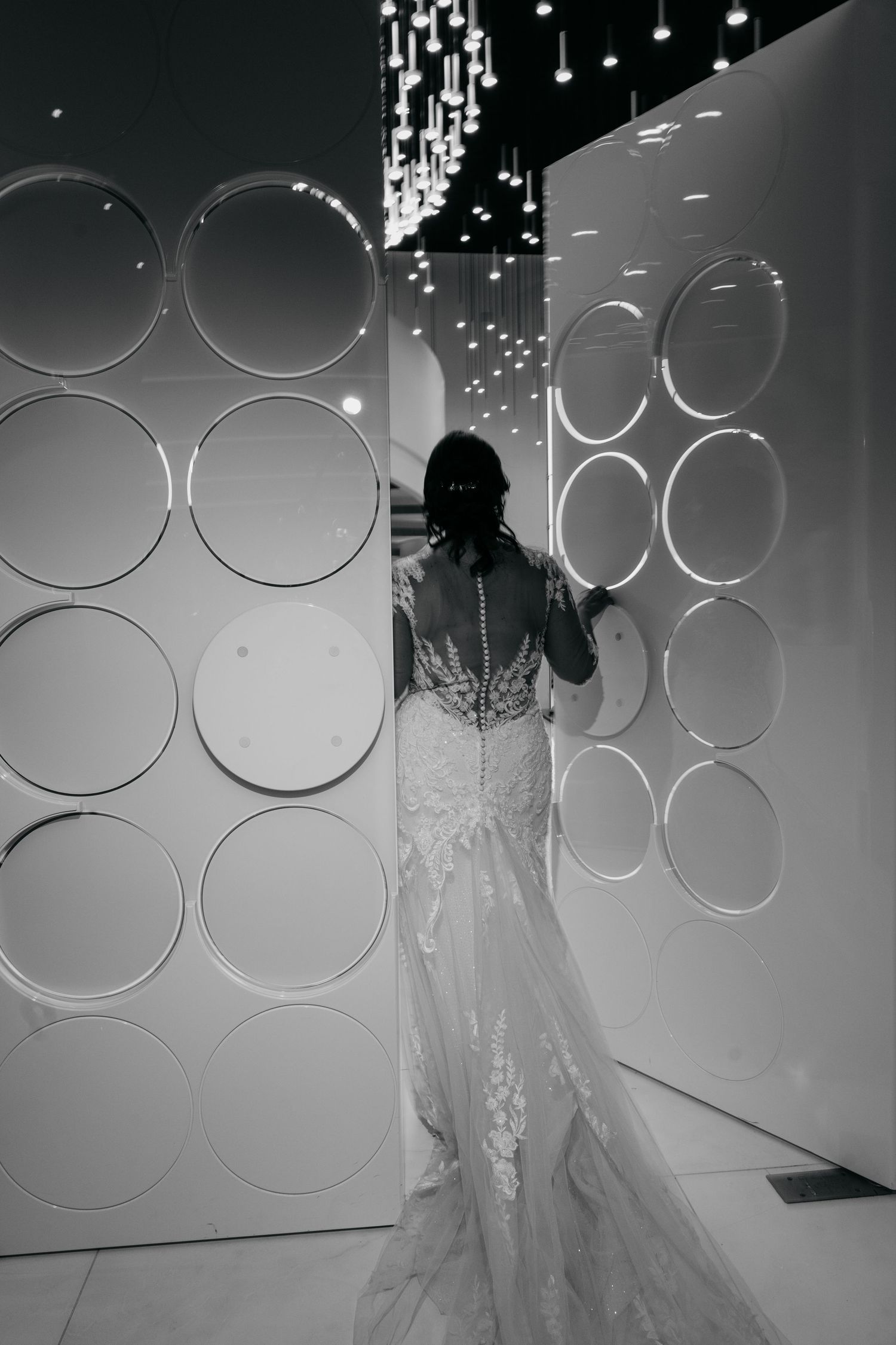 Artistic black and white wedding photo with circular light patterns and flowing gown silhouette.