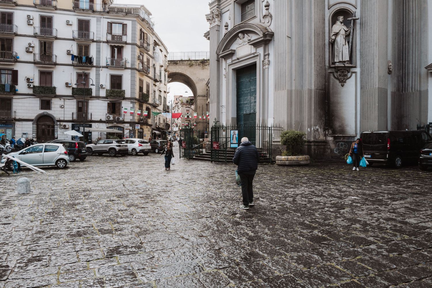 Historic city square with cathedral archways and cobblestone streets in Naples, Italy.
