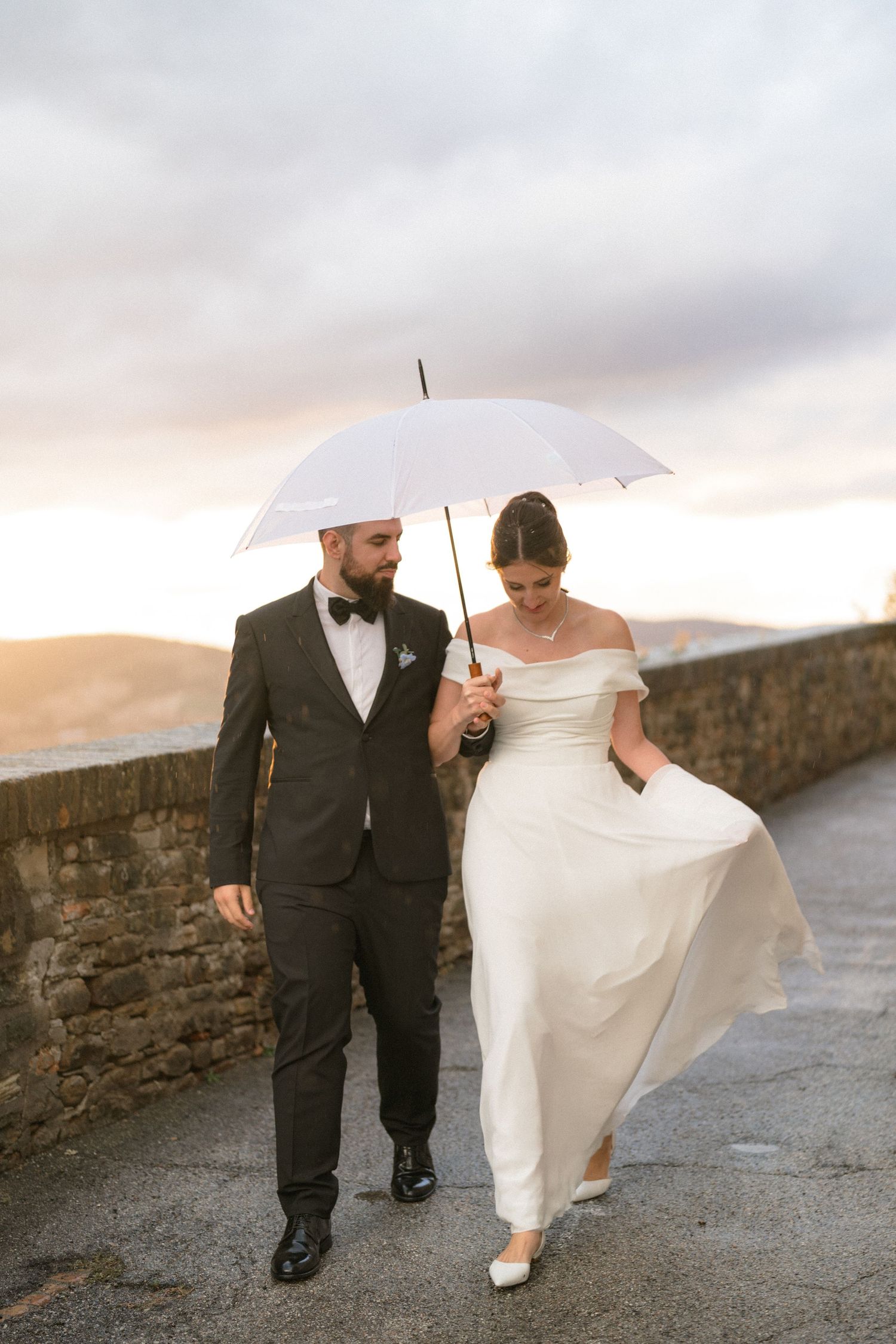 A couple walks together under a white umbrella on a cloudy day.