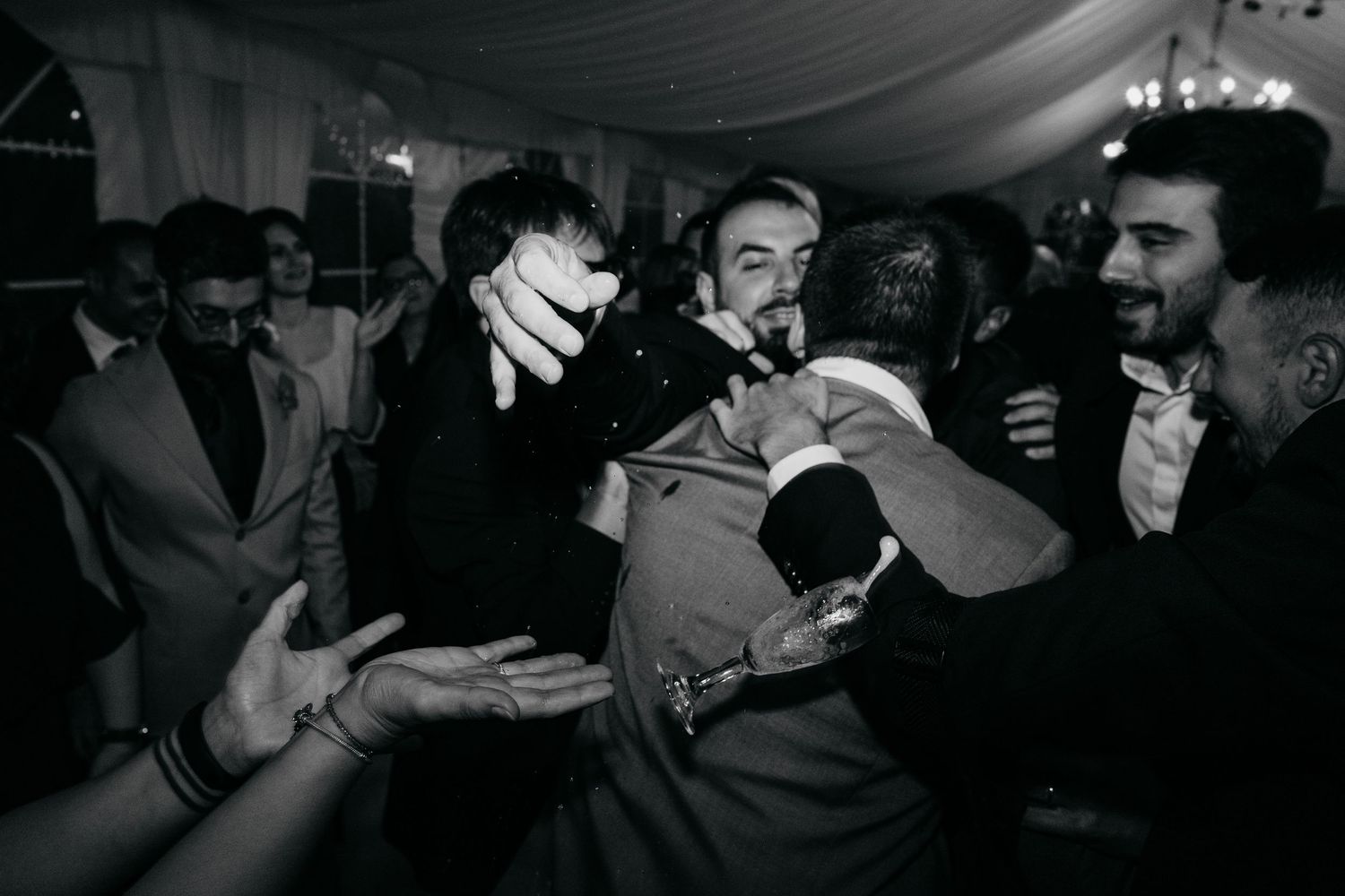 Dark reception venue with guests dancing and celebrating in low light.