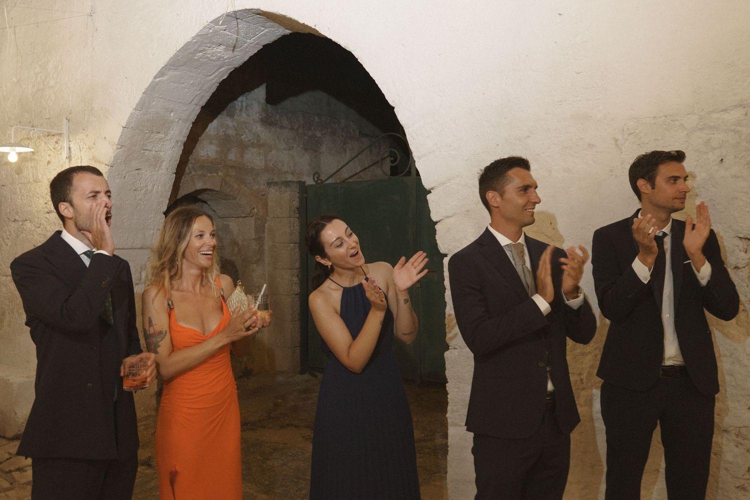 A group of wedding guests cheering and celebrating under a stone archway.