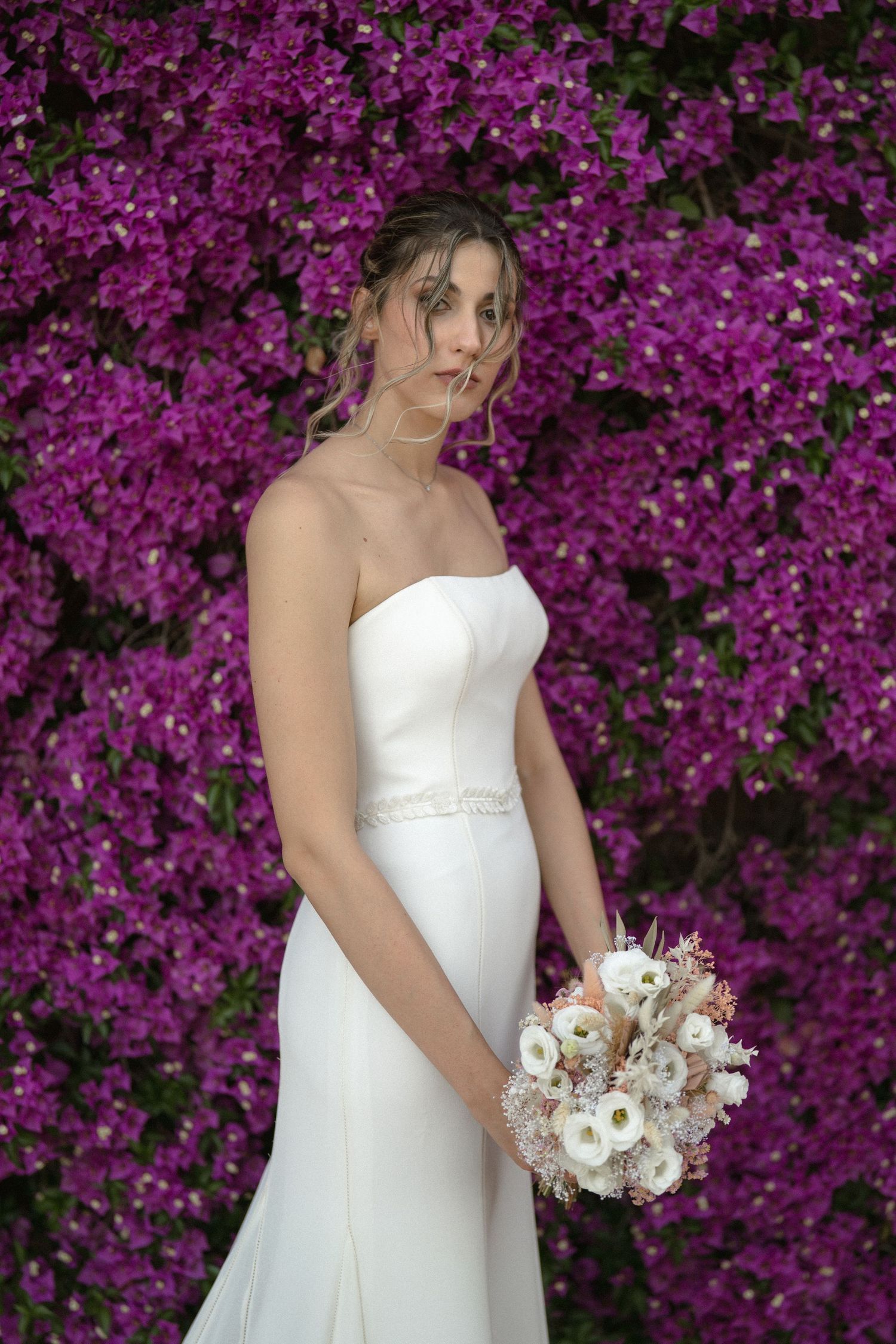 White wedding dress and bouquet photographed against vibrant purple bougainvillea flowers.