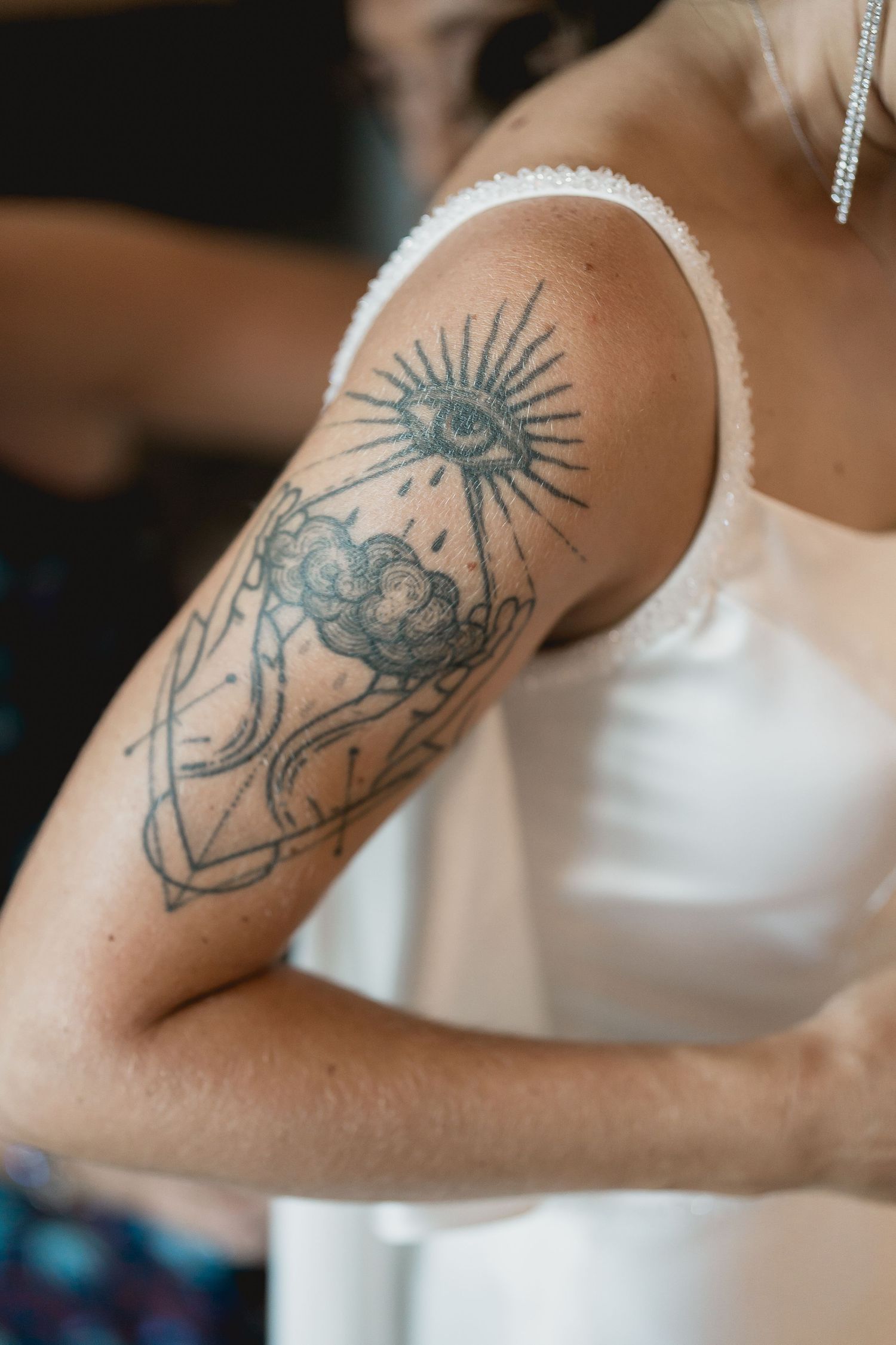 An artistic tattoo featuring a sun and clouds design visible on a bride's arm in her wedding dress.