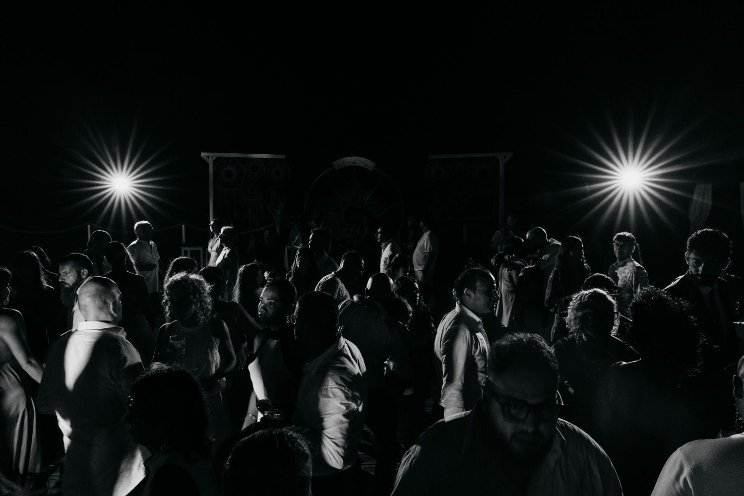 Dark silhouettes of wedding guests dancing at a nighttime reception.