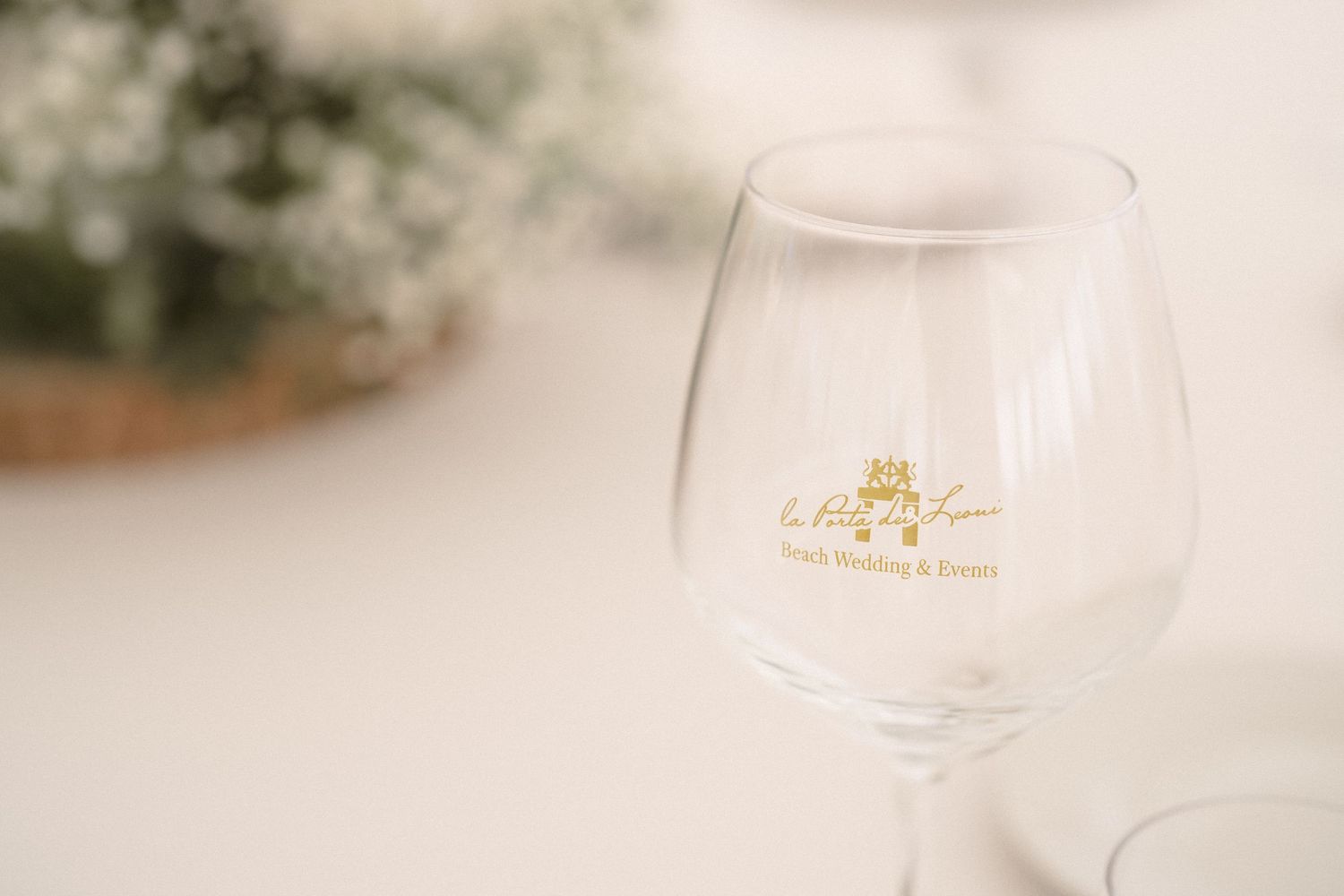 Close-up of an elegant wine glass with a gold logo detail against a soft white background.