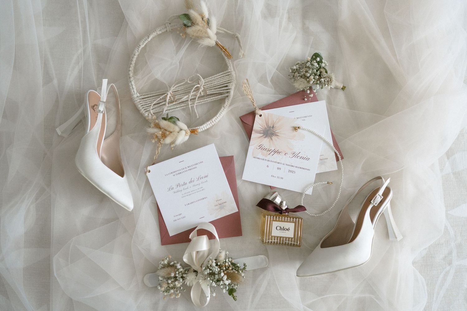 Delicate wedding details including white floral arrangements, ribbons, and invitation cards arranged on a light surface.