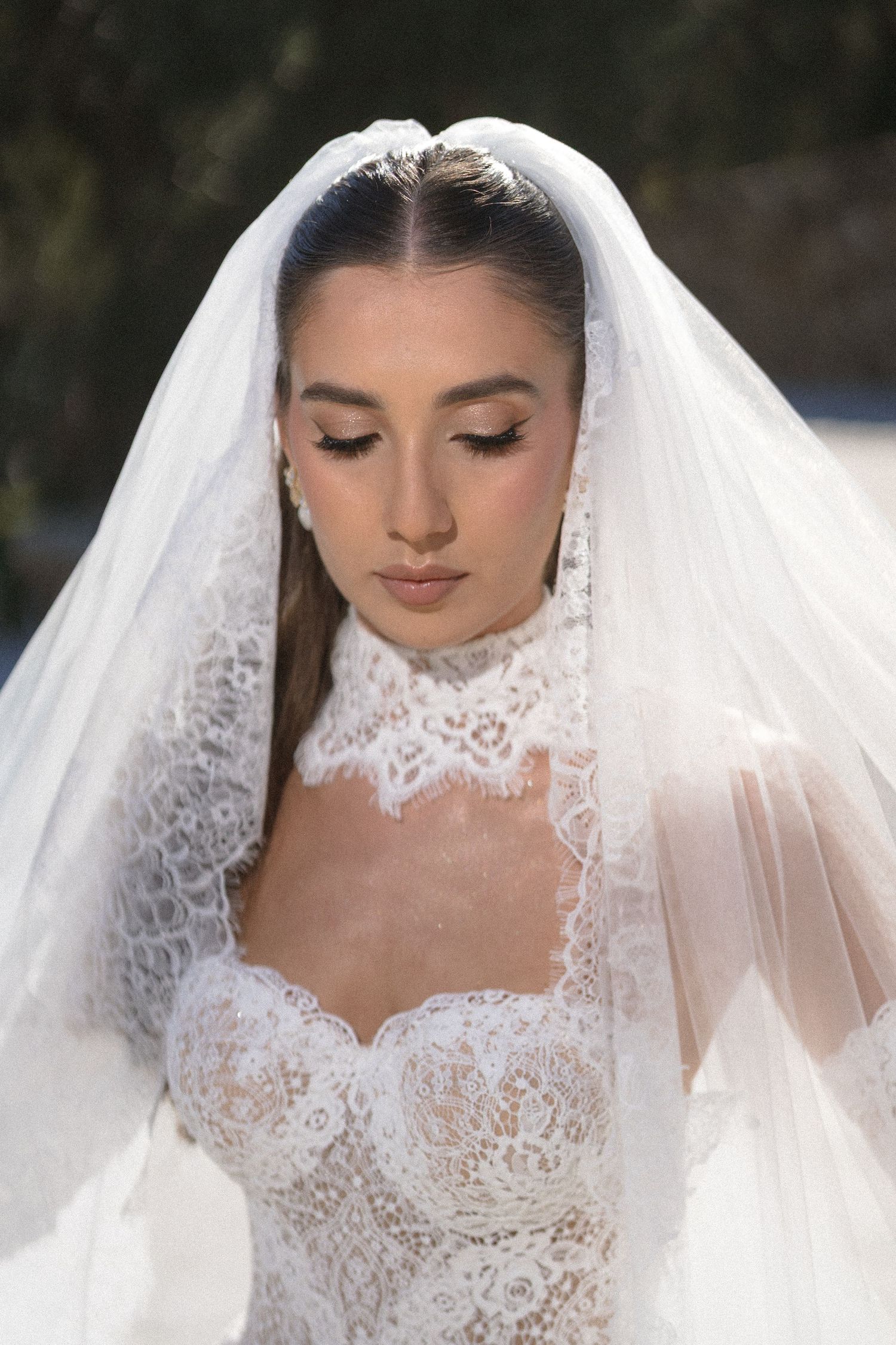 Close-up of a bride with eyes lowered, wearing a sheer veil and a lace gown with a high lace collar.