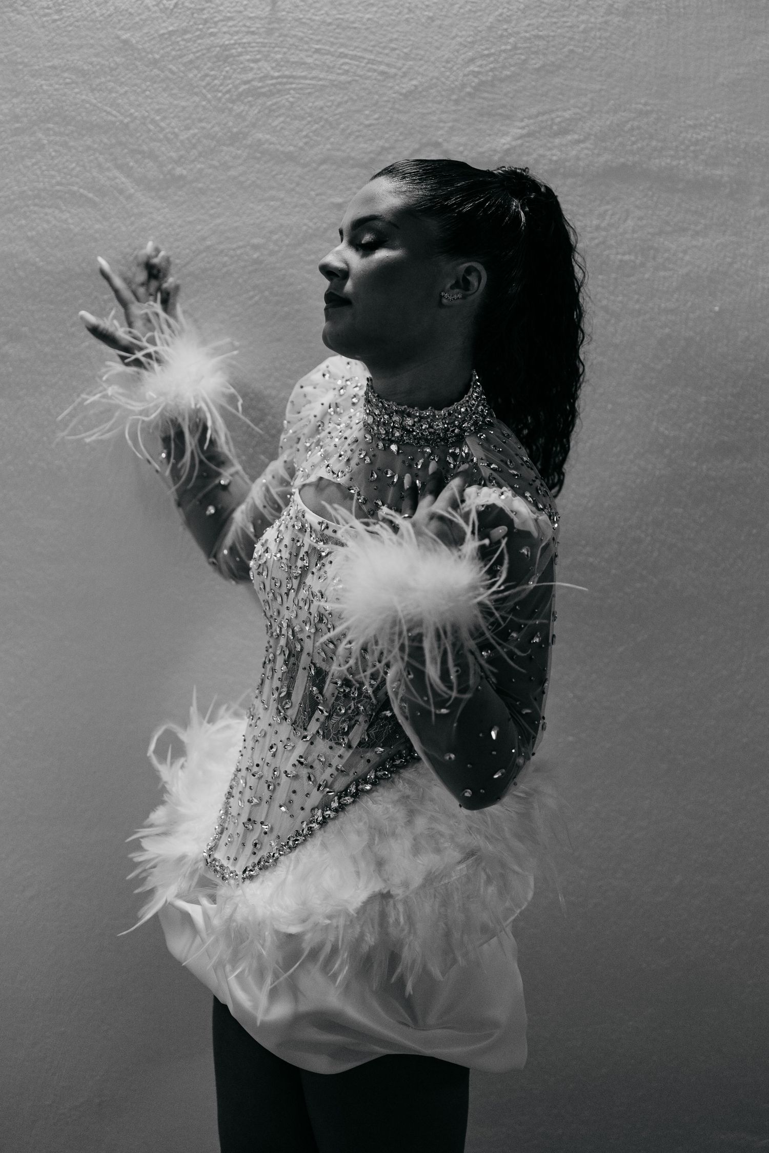 Black and white photo of a woman in a beaded, feather-trimmed costume posing gracefully against a light background.