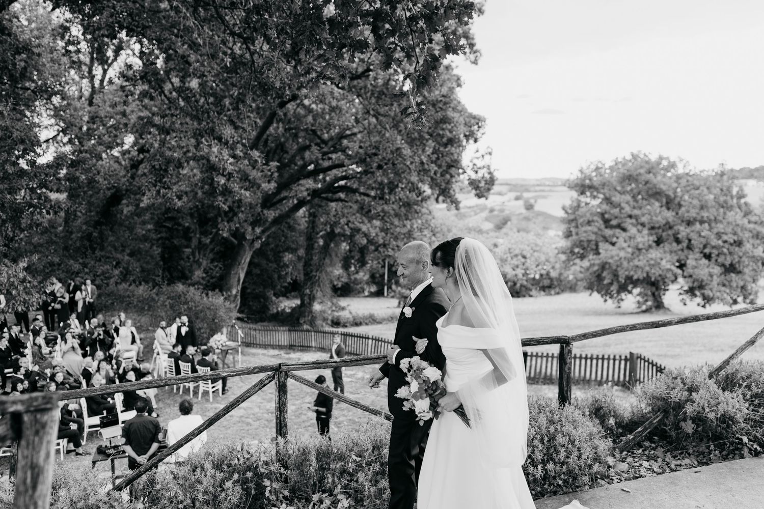 A wedding ceremony takes place on a scenic overlook with trees and natural surroundings.