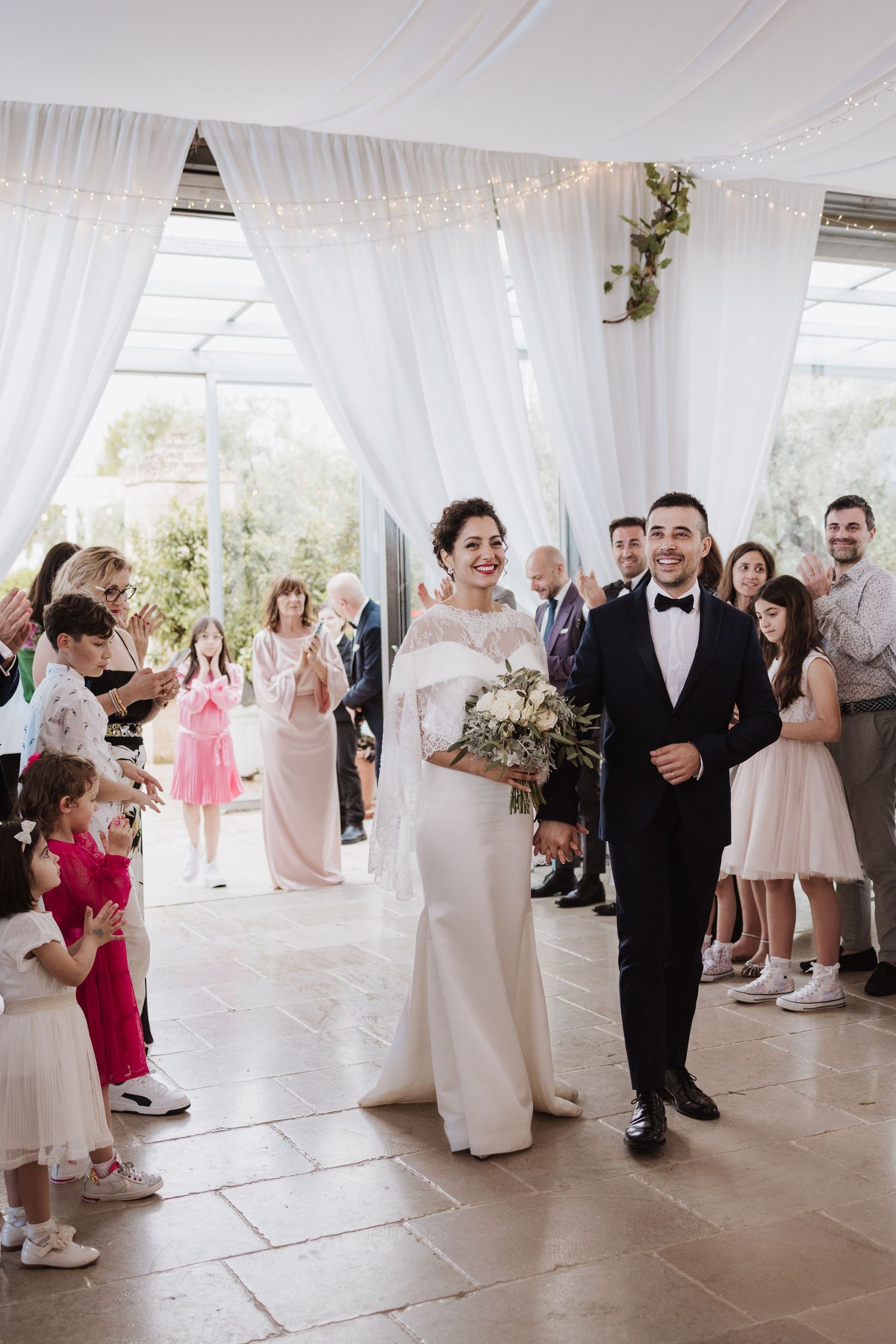 Wedding ceremony exit with couple walking through white draped venue surrounded by guests.