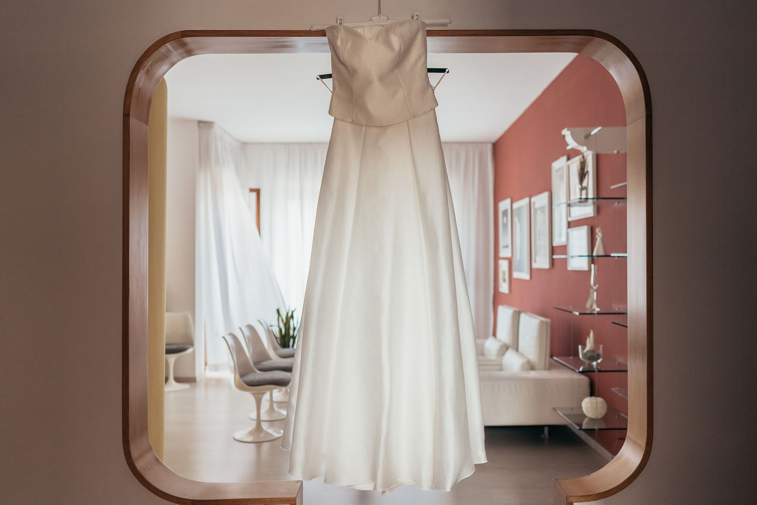 White wedding dress hanging in an arched doorway with coral walls.