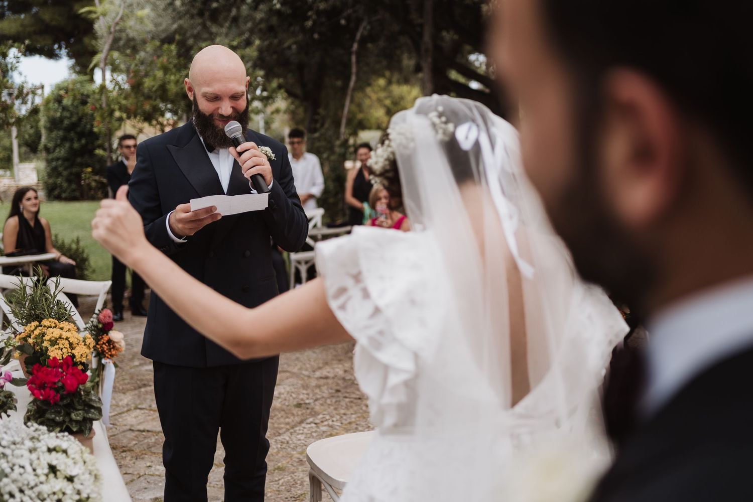 Wedding vow exchange during outdoor ceremony with traditional white decor and natural backdrop.