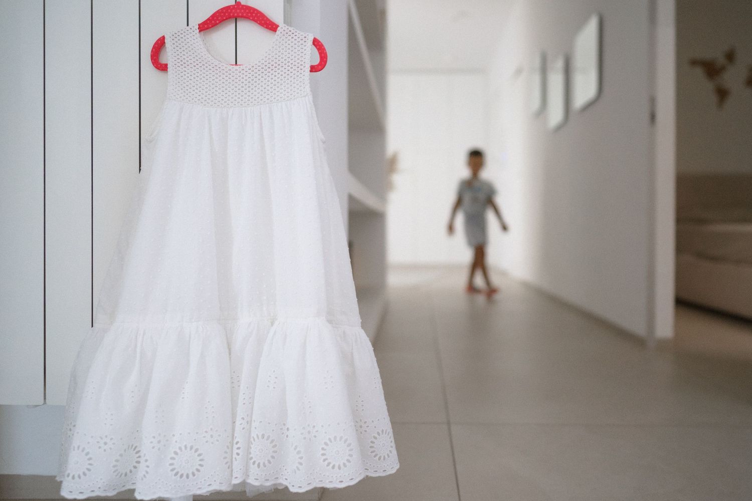 A white wedding dress hangs elegantly in a bright hallway, showcasing its delicate lace details and flowing silhouette.