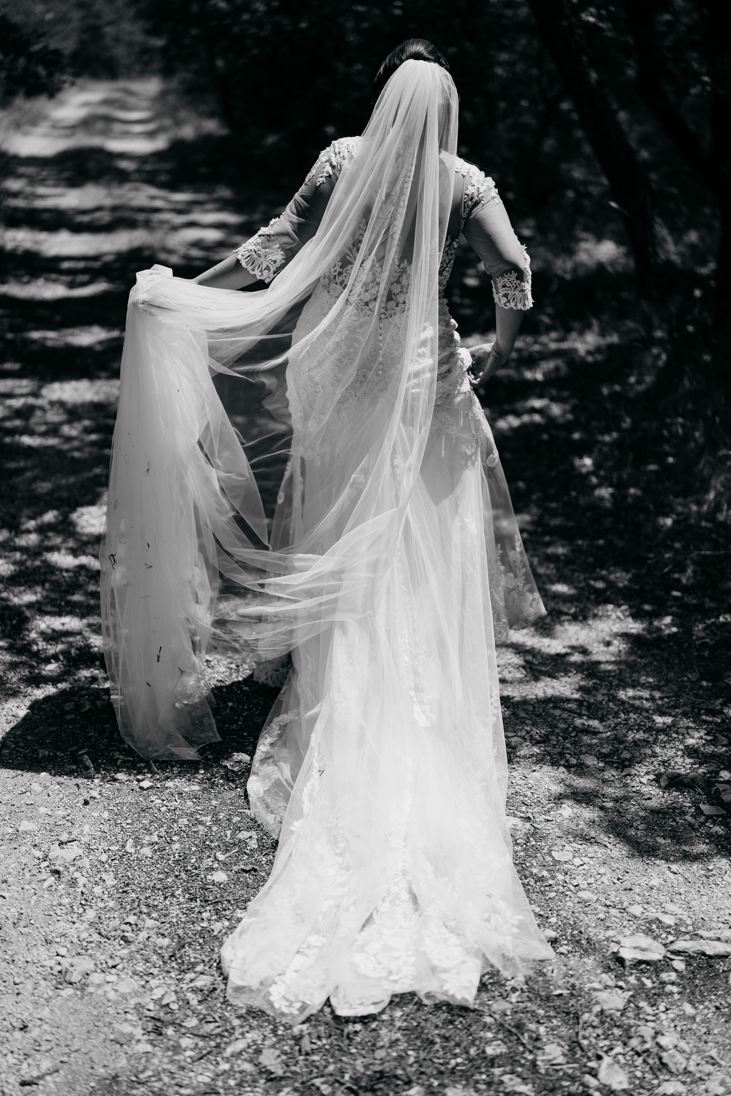 Flowing white wedding dress veil trailing behind on a natural outdoor path in black and white.