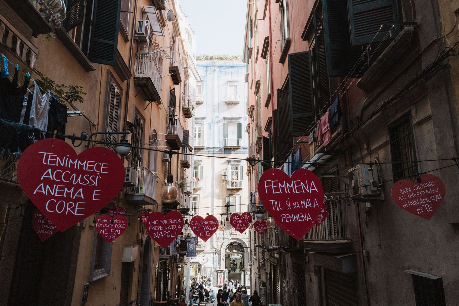 Pink decorative signs hang across a narrow alleyway between pink Mediterranean buildings in an urban setting.