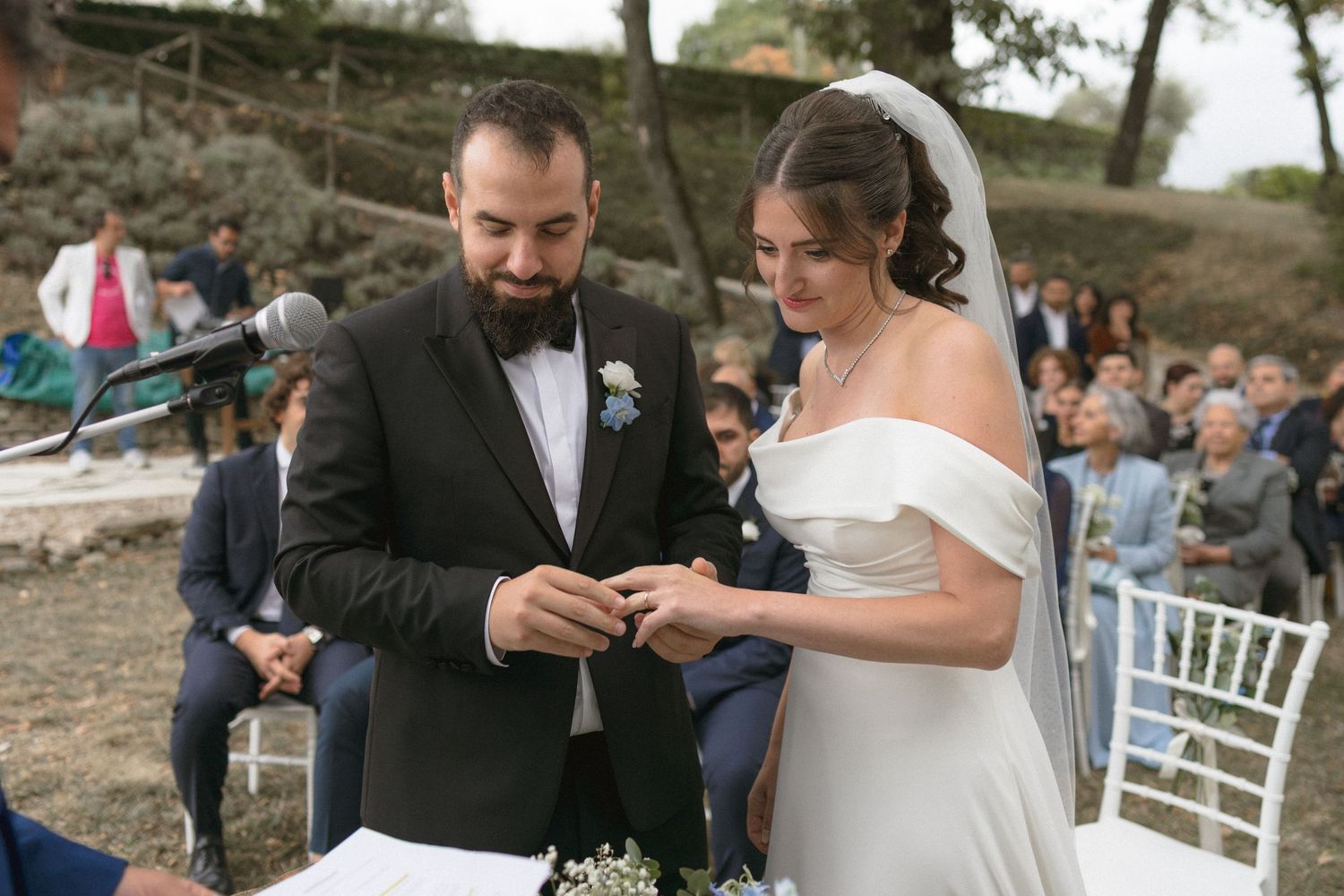 Wedding ceremony moment showing exchange of rings in an outdoor garden setting.