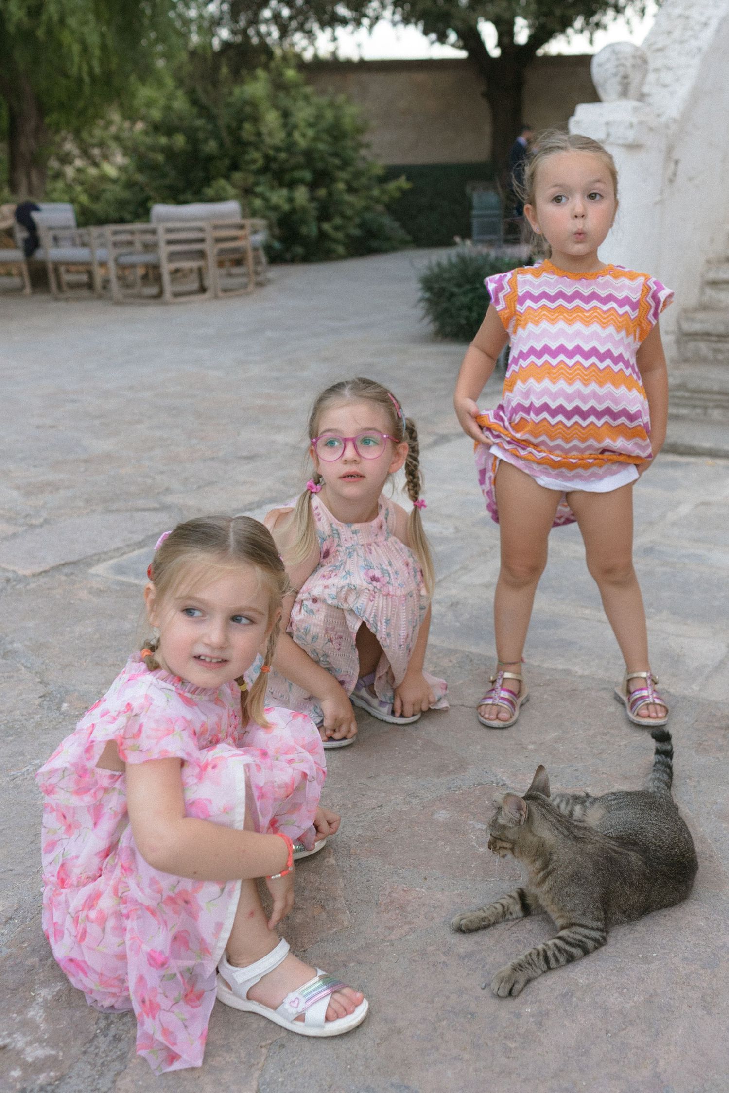 Children interacting with a gray tabby cat on a stone patio.