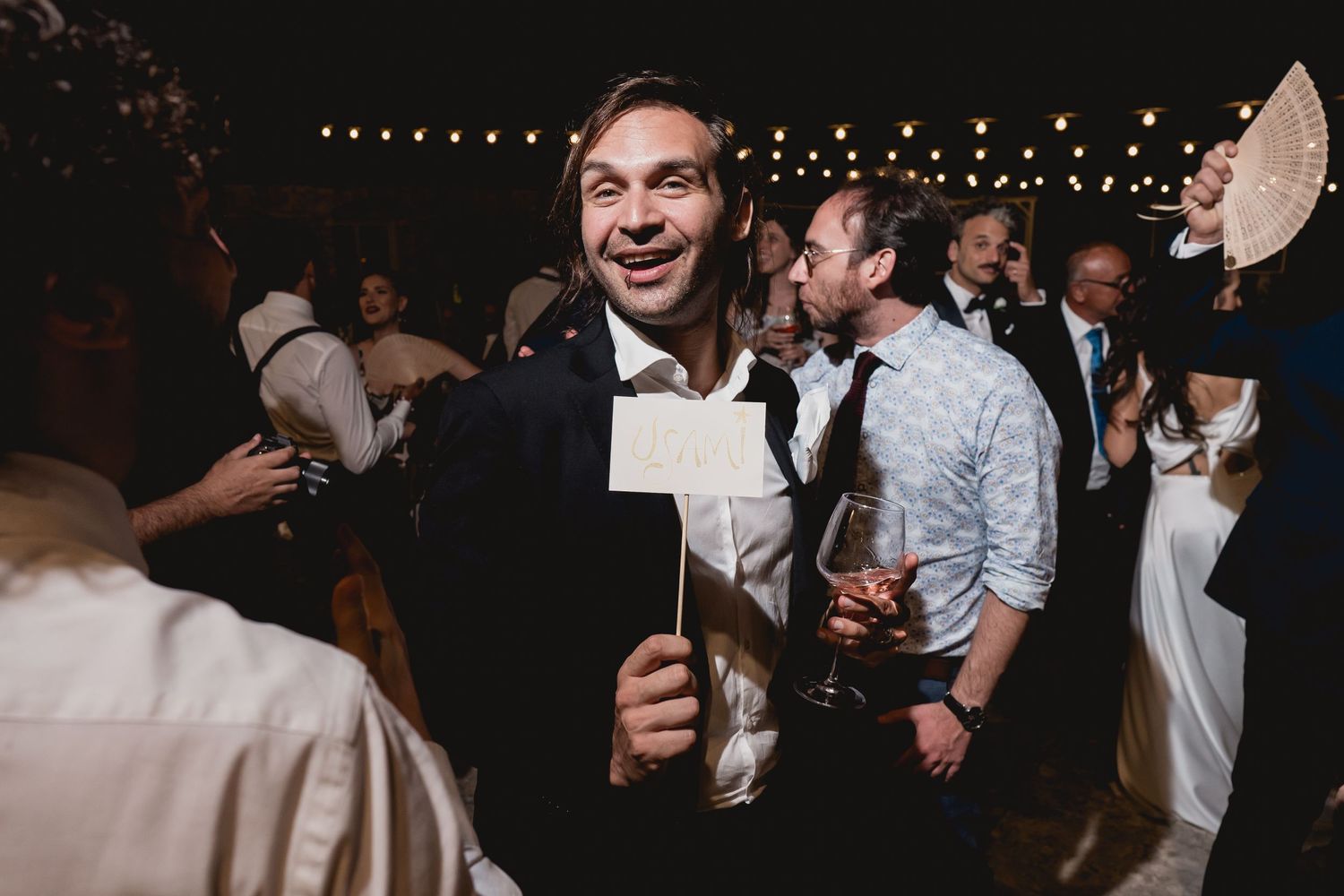 Party guests celebrate on a lively dance floor at a wedding reception with string lights overhead.
