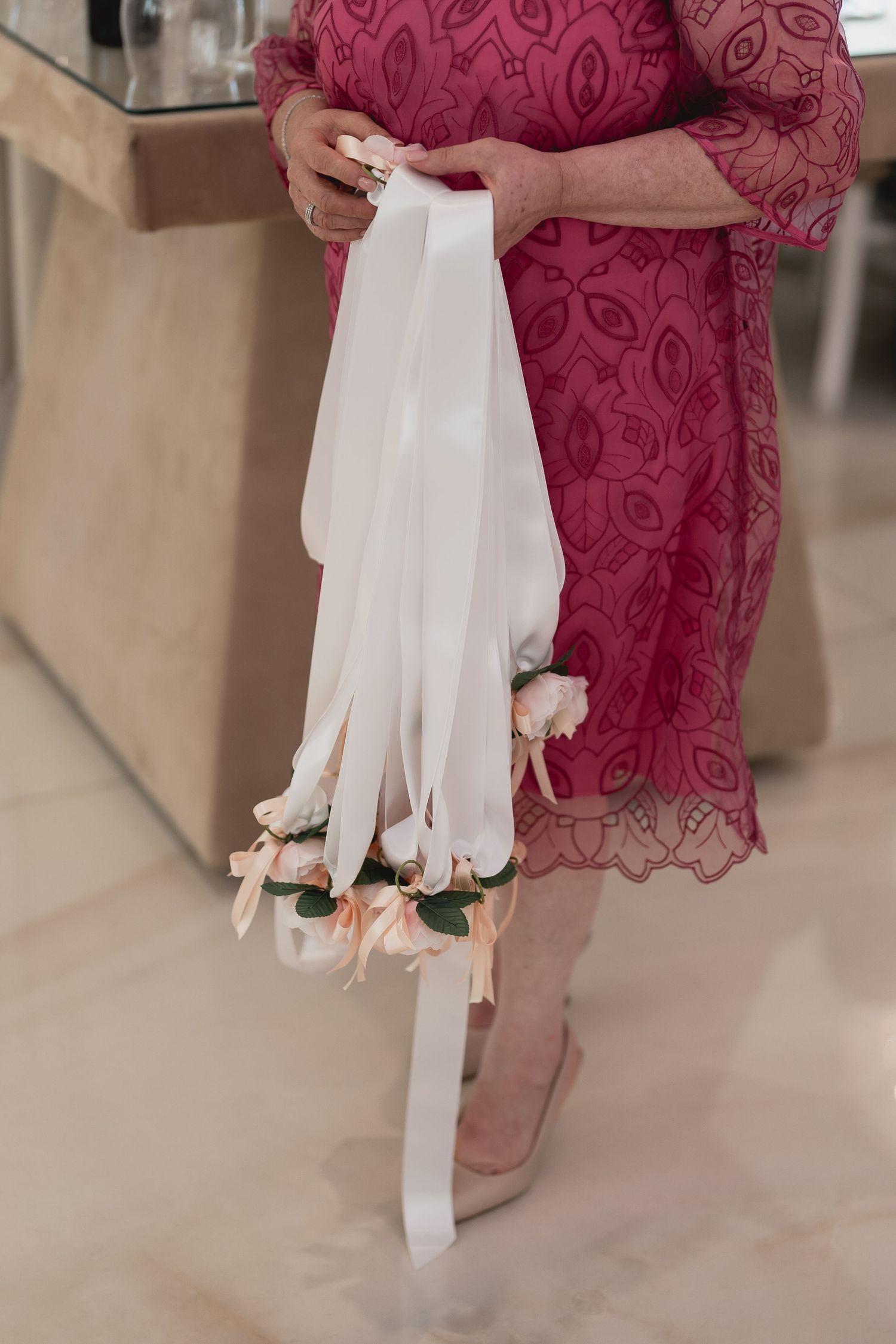 Person in burgundy lace dress holding white ribbons with floral decorations.