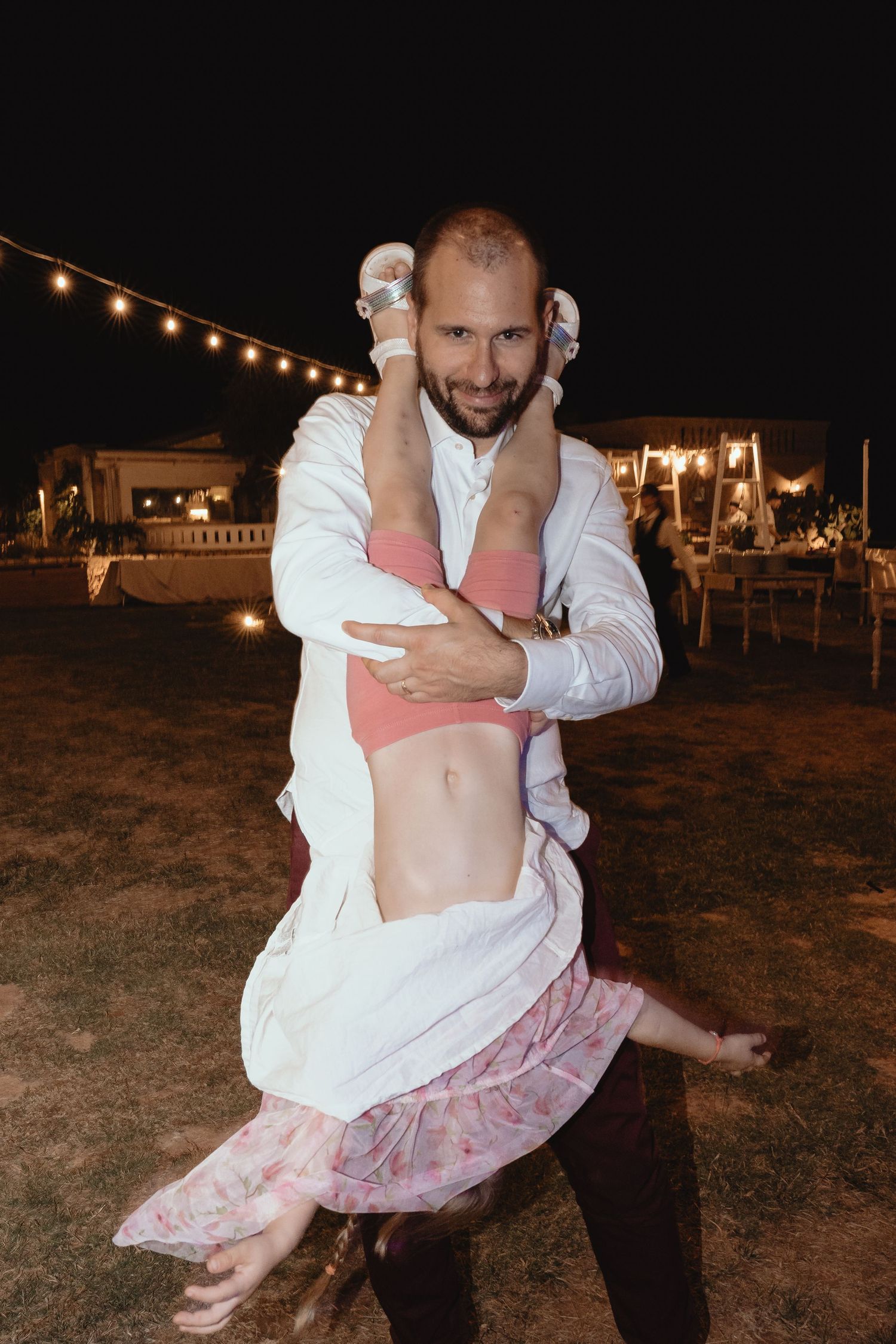 Couple dancing at an outdoor evening reception with string lights visible in the background.