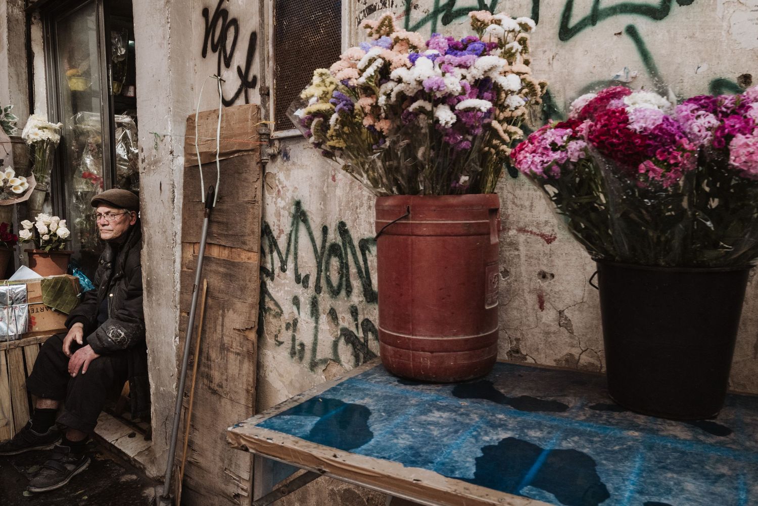 Colorful flower arrangements in pots next to graffiti-covered wall in urban setting.