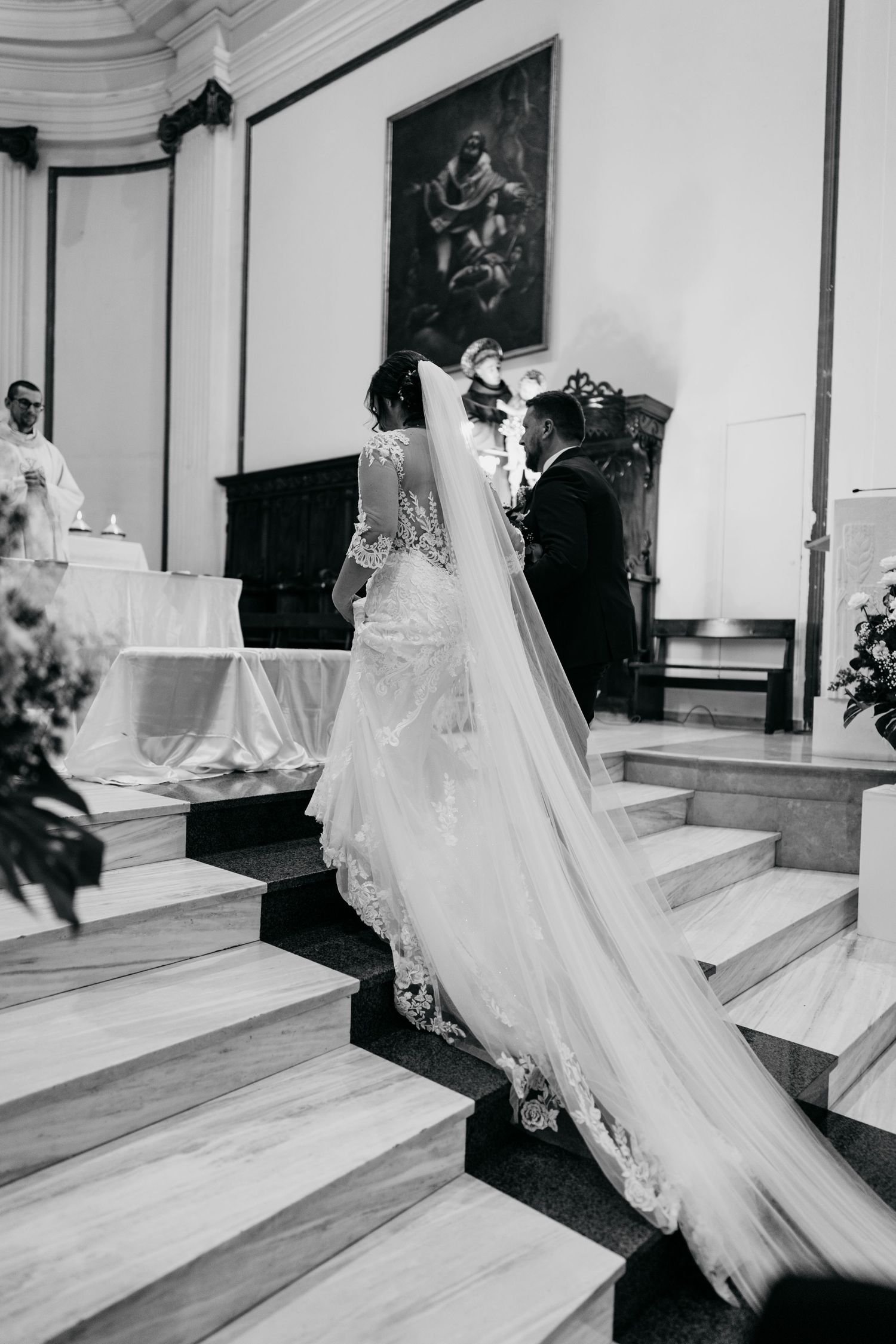 A flowing white wedding veil trails elegantly down a grand staircase in a black and white photograph.