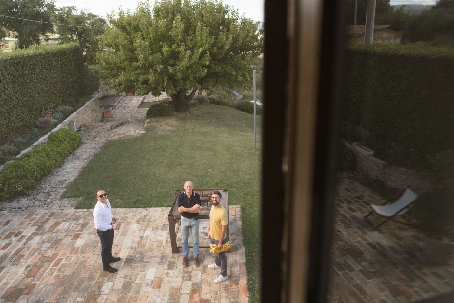 View from above of people standing on a brick patio with lawn and greenery in the background.