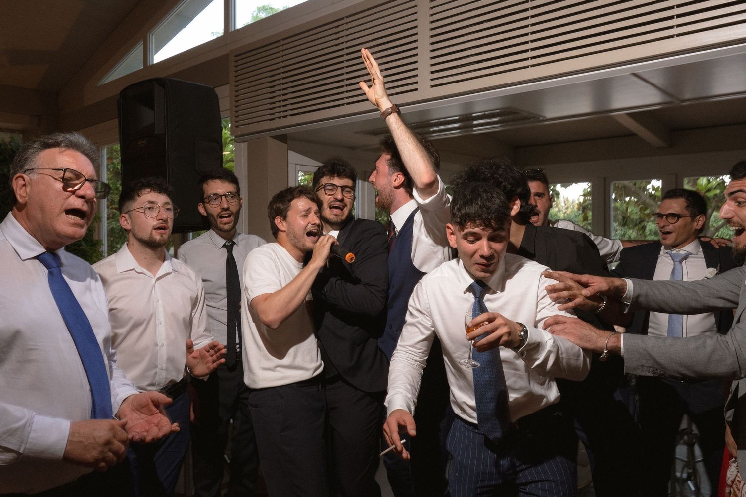 Large group of wedding guests dancing and celebrating in a modern venue with wooden ceiling details.