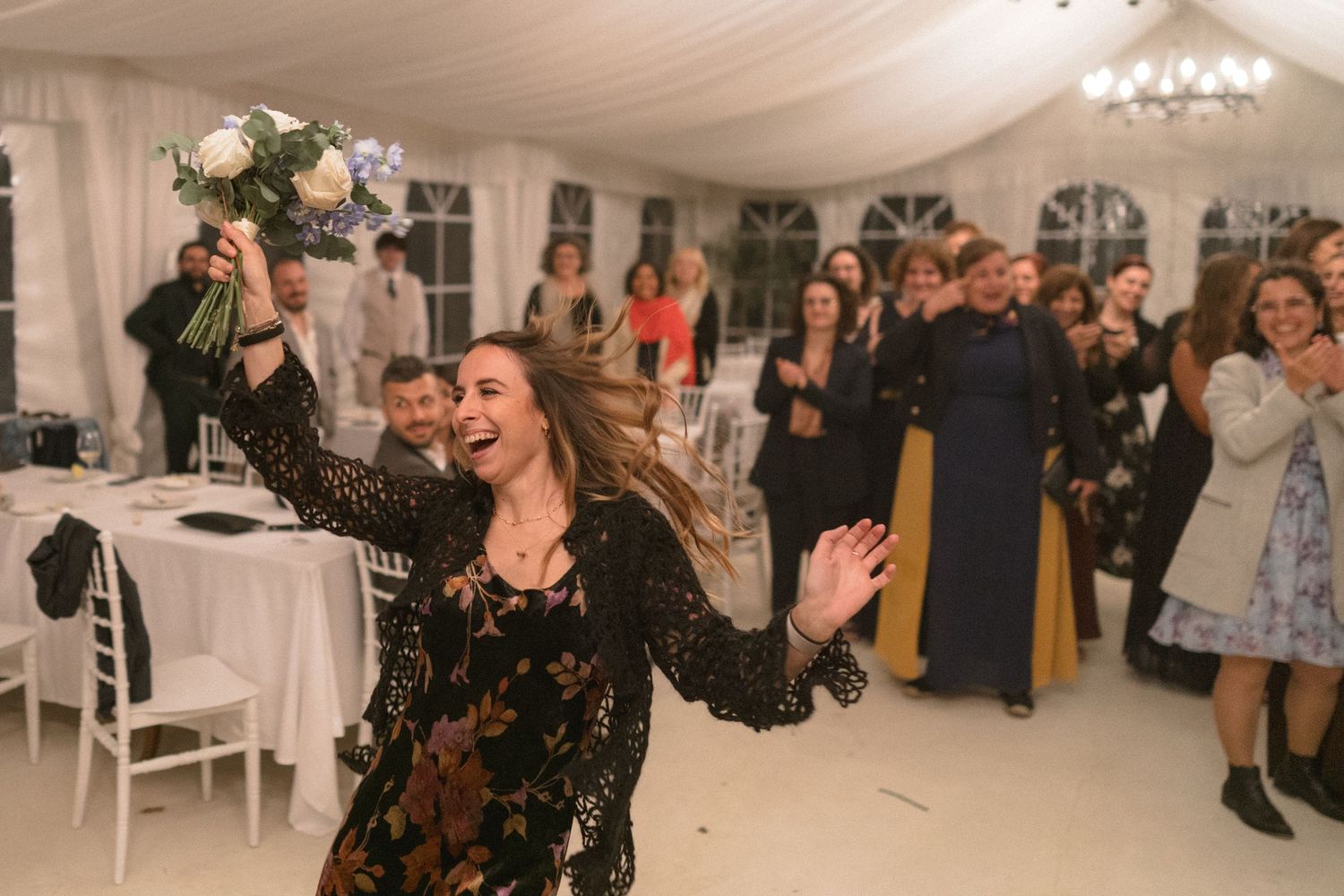Wedding guests dancing and celebrating in a white tent reception venue with elegant draping.