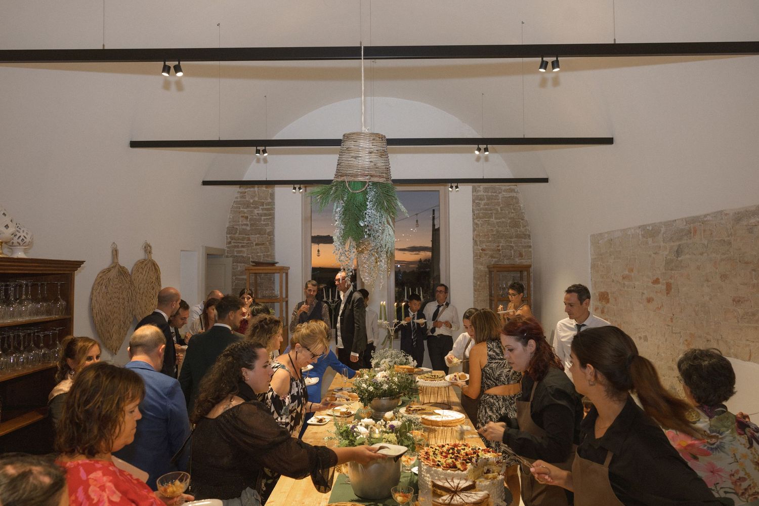 Guests gathered around elegantly set dinner tables at a rustic reception venue with stone walls and chandeliers.