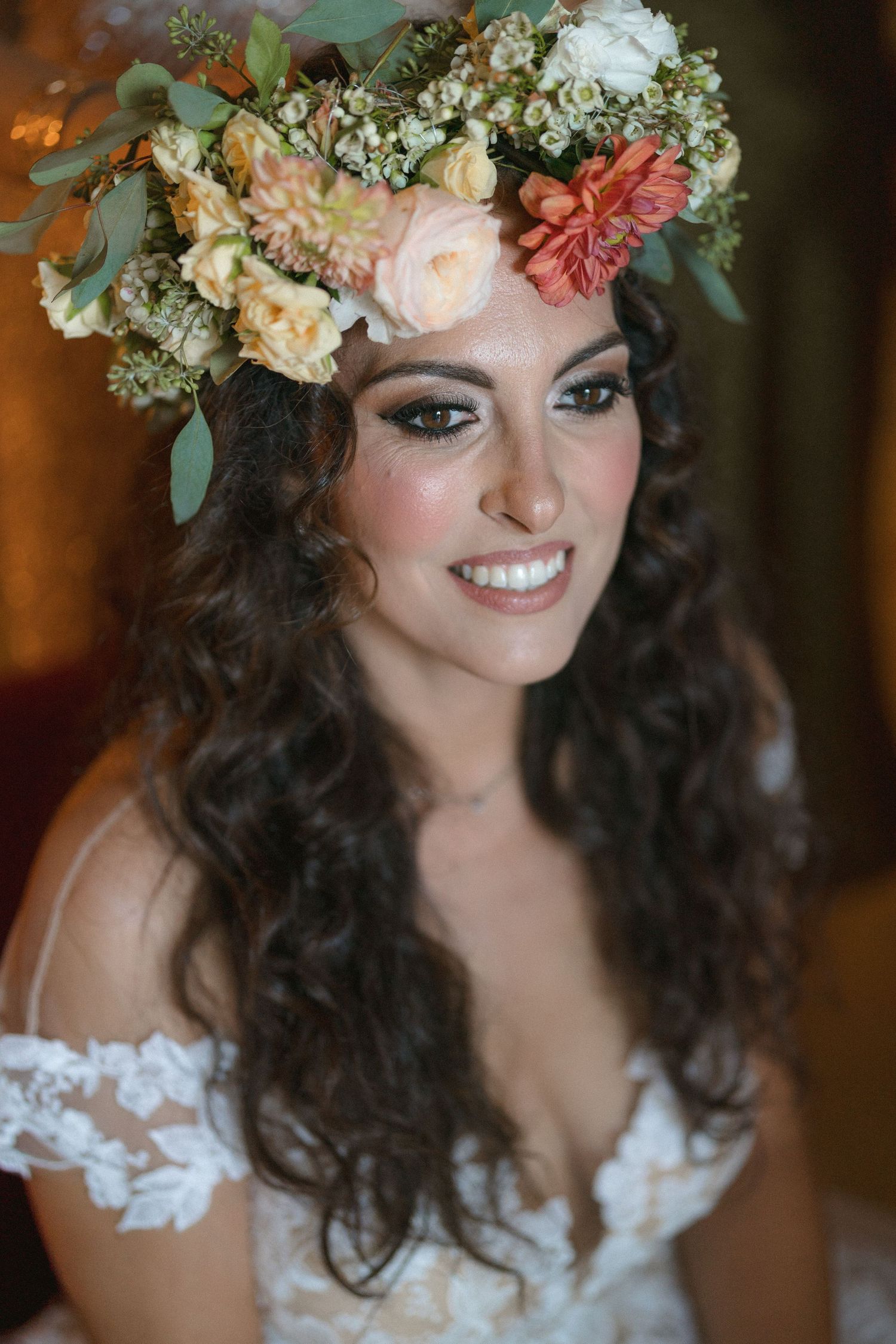 Bride wearing a delicate floral crown and lace dress smiles warmly.