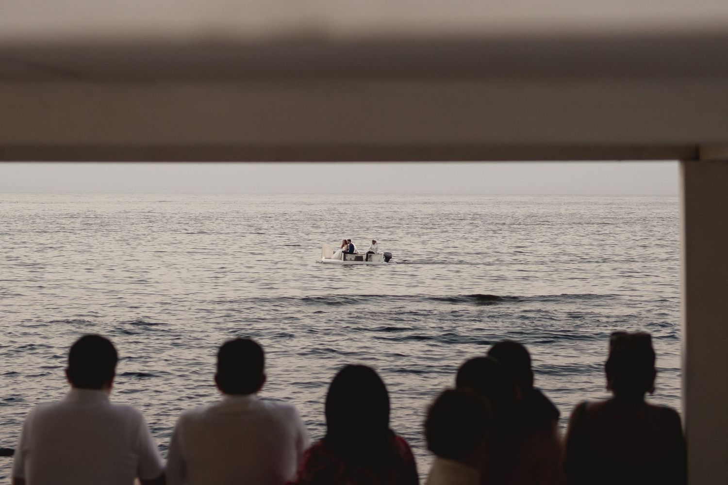 Silhouettes of wedding guests watching distant swimmers in the ocean.