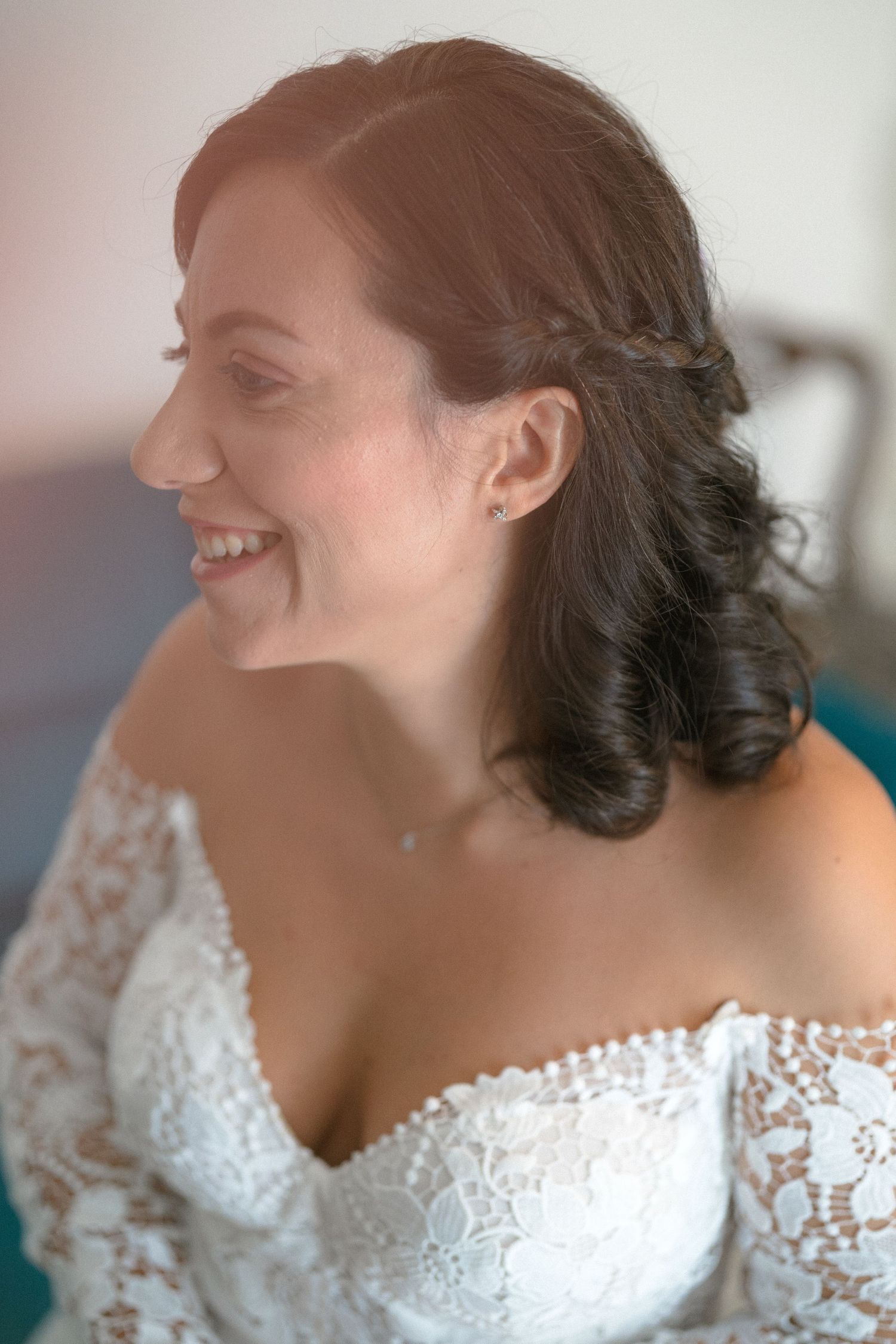 Close-up profile views of someone wearing a delicate white lace wedding dress with an off-shoulder neckline.