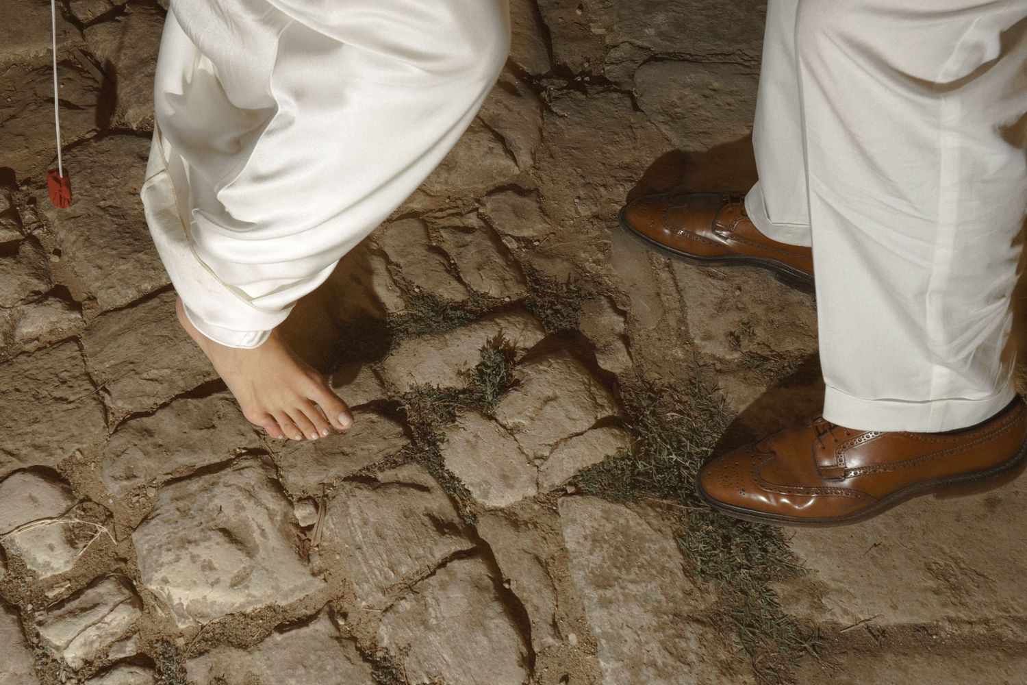 Contrasting formal brown shoes and bare feet on stone pathway during wedding celebration.