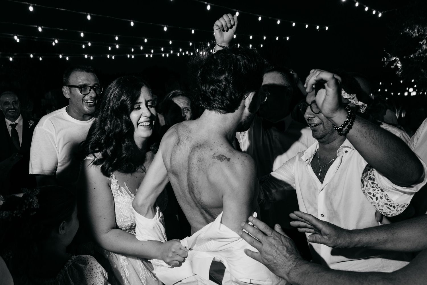 Wedding reception guests laughing and celebrating together at a party under string lights.