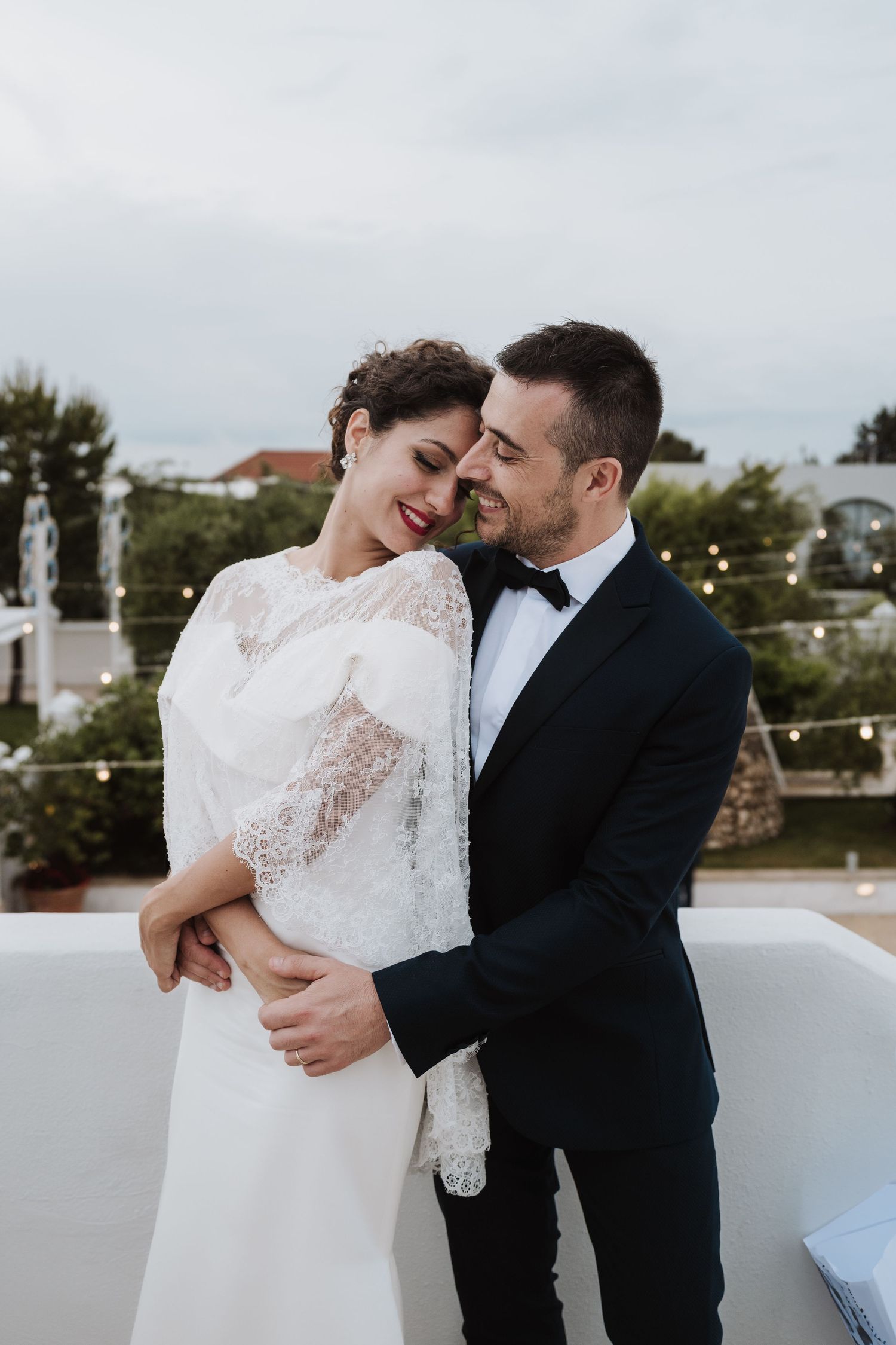 Romantic wedding moment captured as couple embraces on an outdoor terrace.