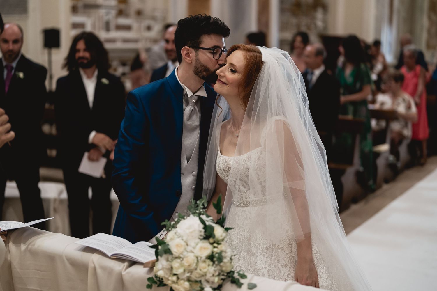 A tender moment between newlyweds at the altar with a white floral bouquet in the foreground.
