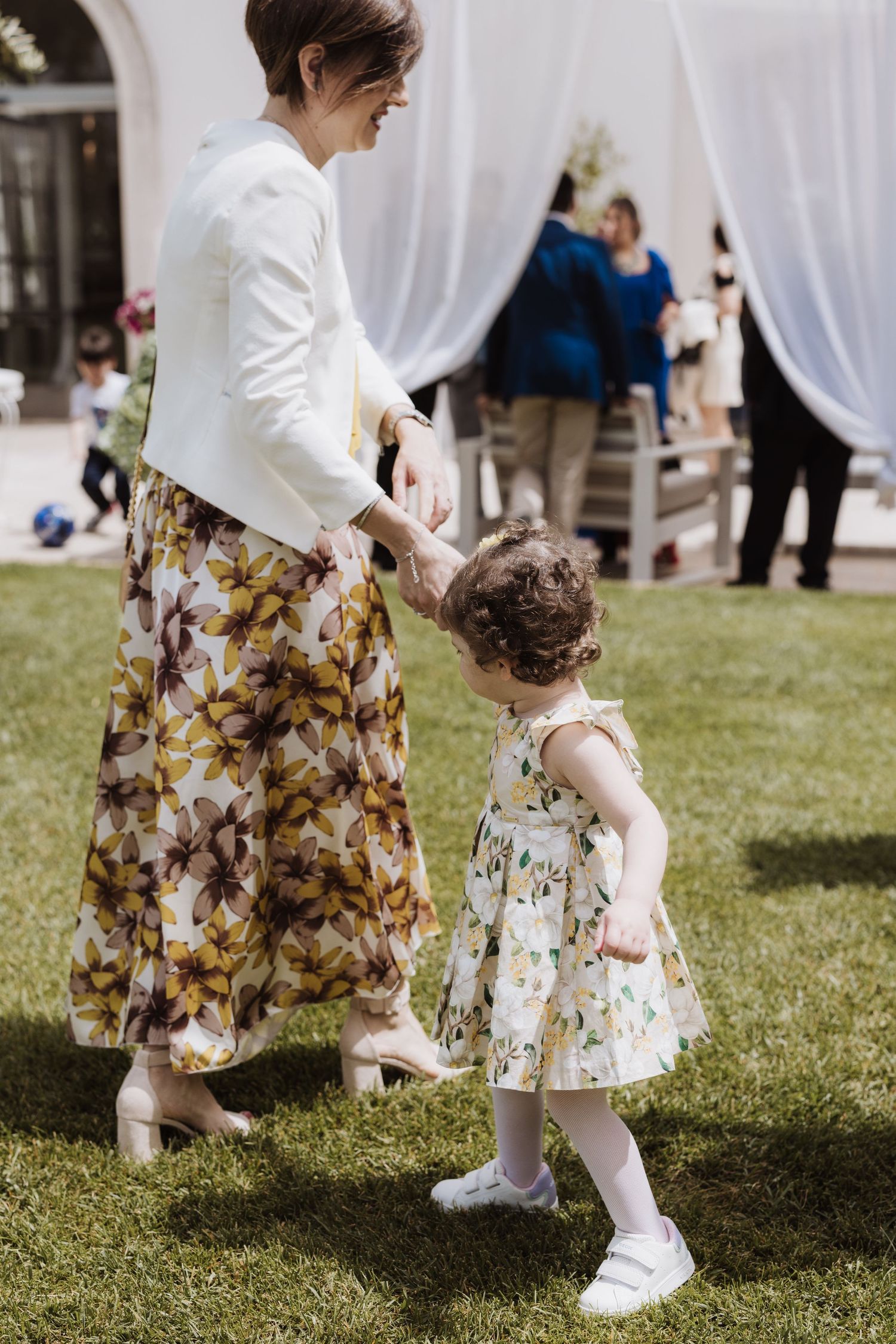 Sweet moment between two people wearing floral dresses at an outdoor wedding.