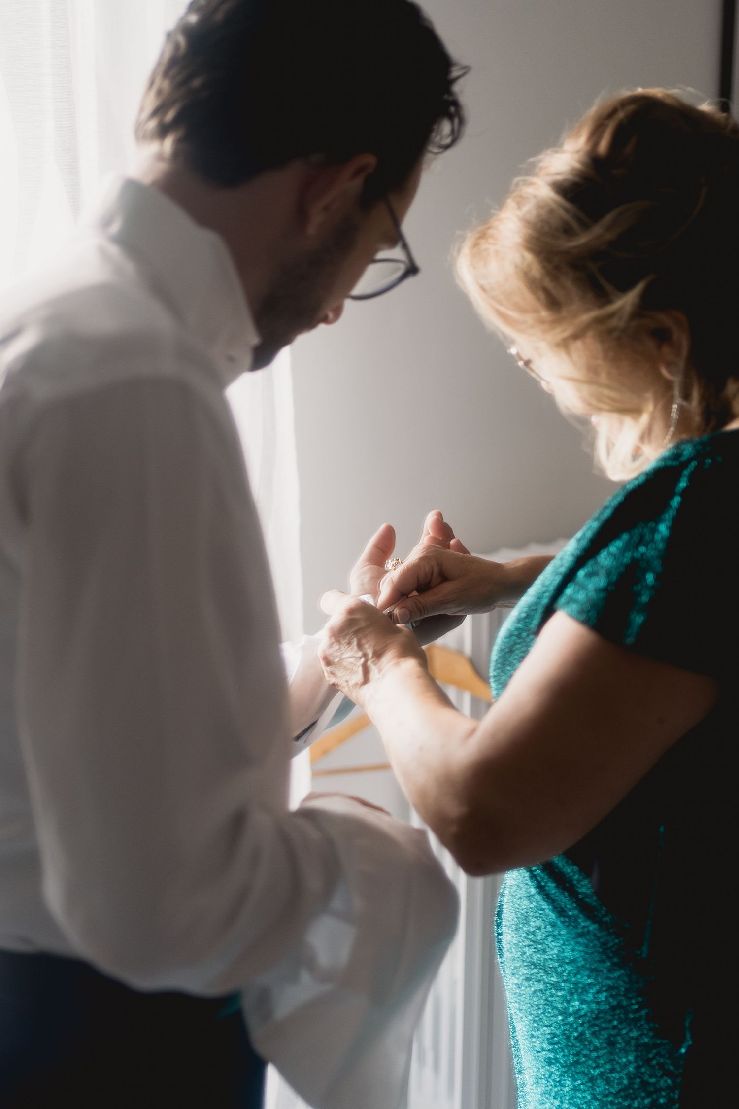 Close up of hands adjusting cufflinks in soft natural window light.