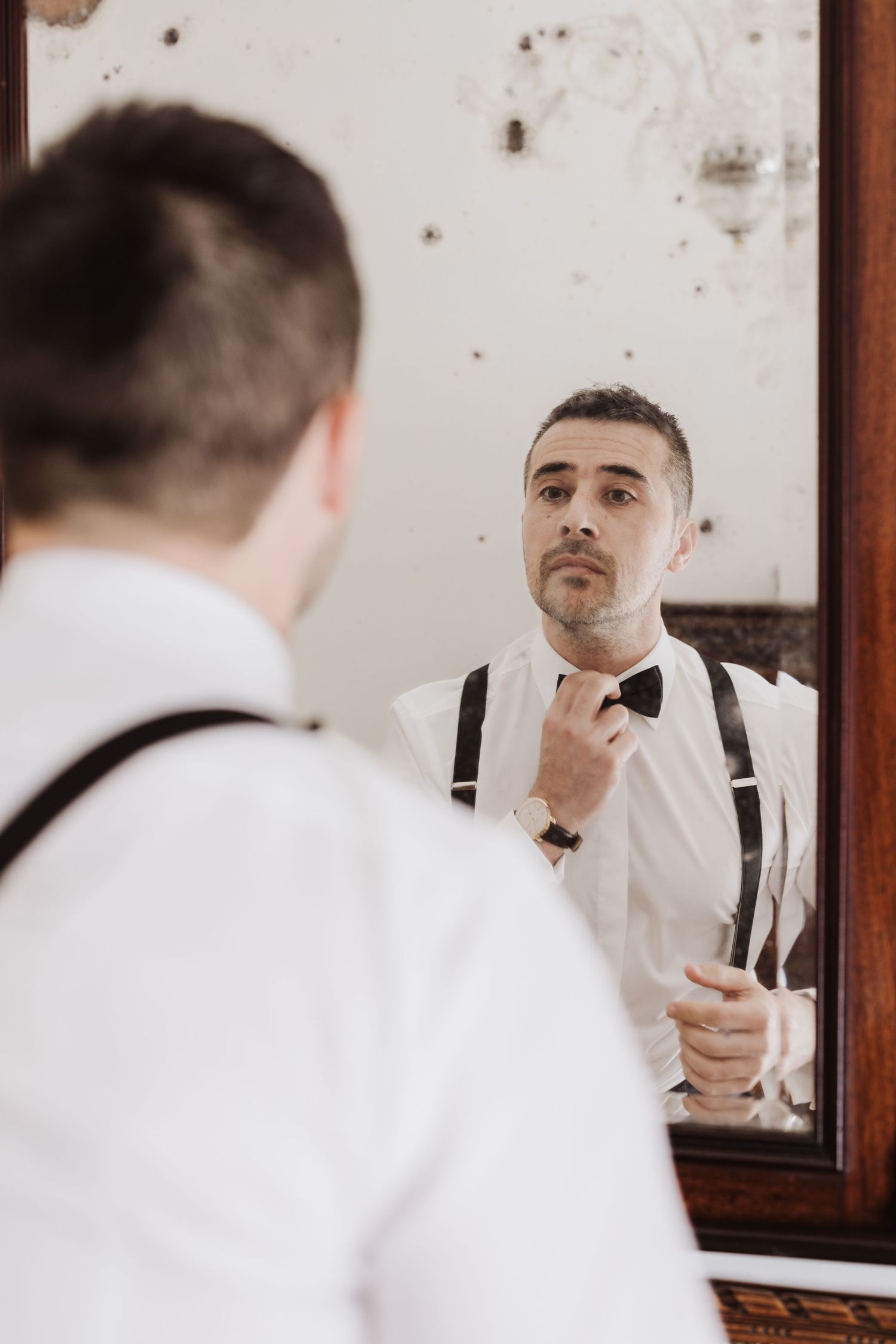 Reflection in vintage mirror shows formal attire being adjusted.
