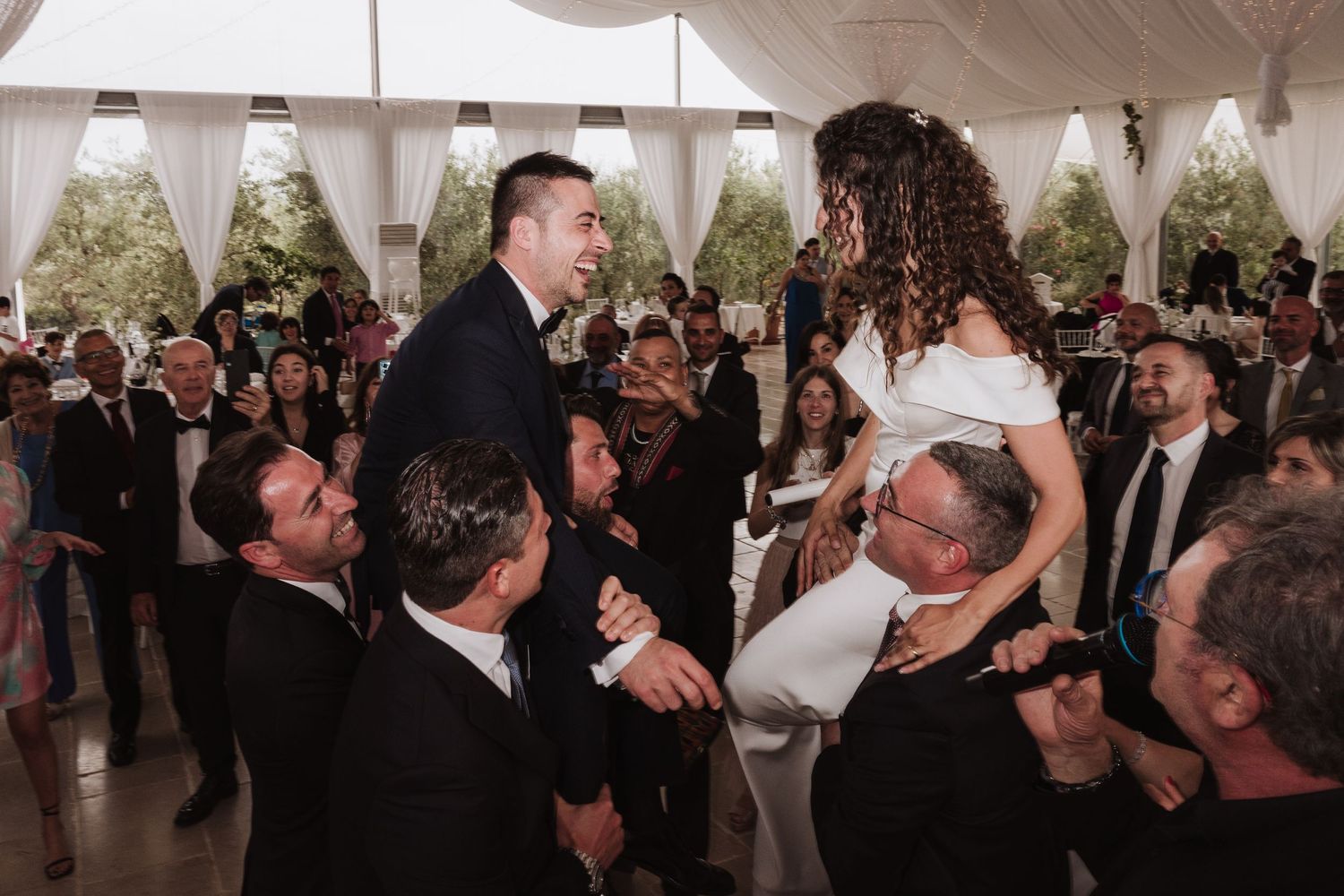 Wedding reception celebration with couple being lifted by guests during traditional dance.