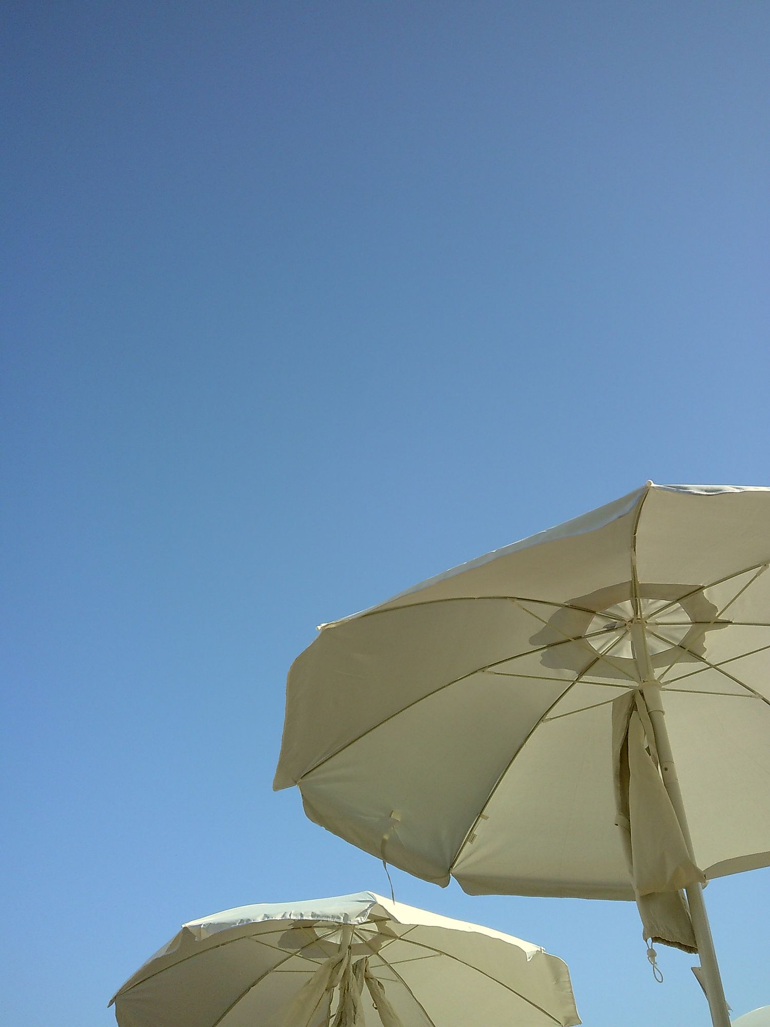 Two white beach umbrellas against a bright blue cloudless sky.